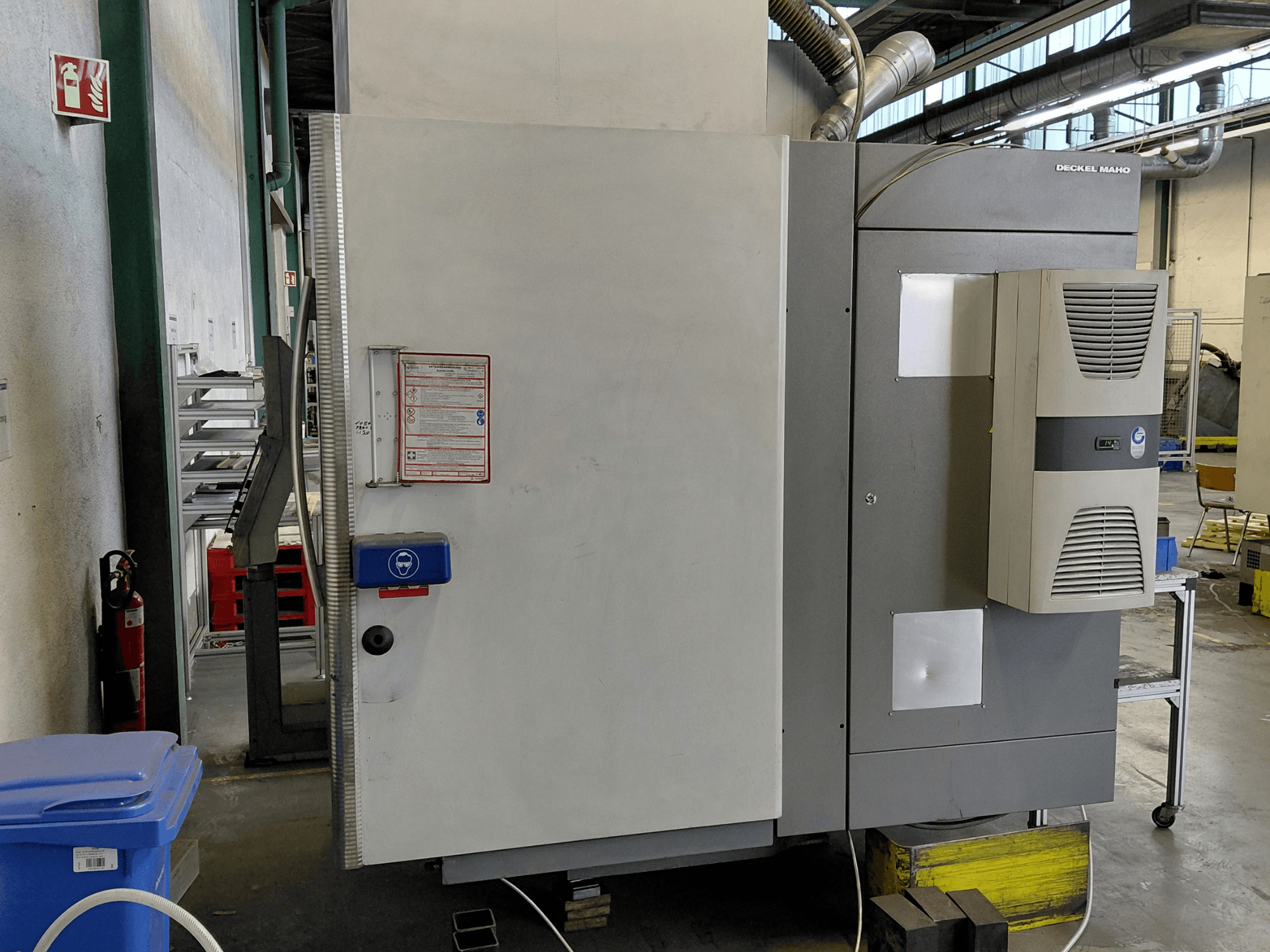 Vue latérale du centre d'usinage vertical DECKEL MAHO DMC 635 V avec le panneau de commande et les étiquettes de sécurité visibles.