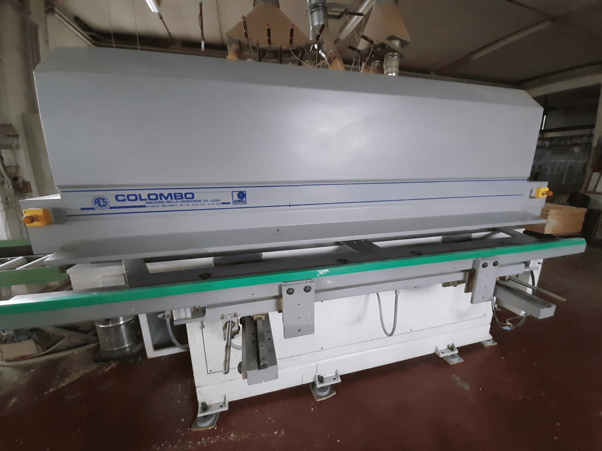 Machine à bois Colombo, vue de face, comportant une longue table verte, des boutons de commande et un corps gris avec des accents bleus.