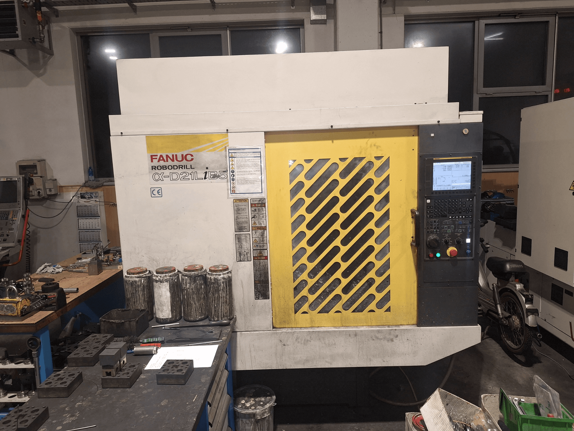 Vue avant de la FANUC Robodrill α-D21LiB5, montrant le panneau de commande, la grille jaune et les outils à proximité sur un établi.