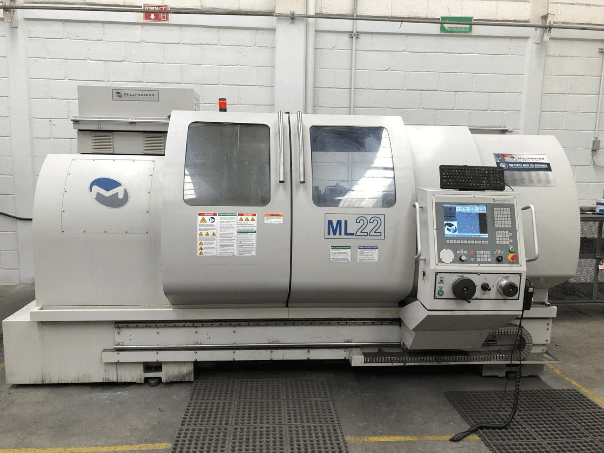 Centre d'usinage vertical MILLTRONICS RH 20, vue de face montrant le panneau de commande, le logo de la marque et les étiquettes de sécurité sur la machine.