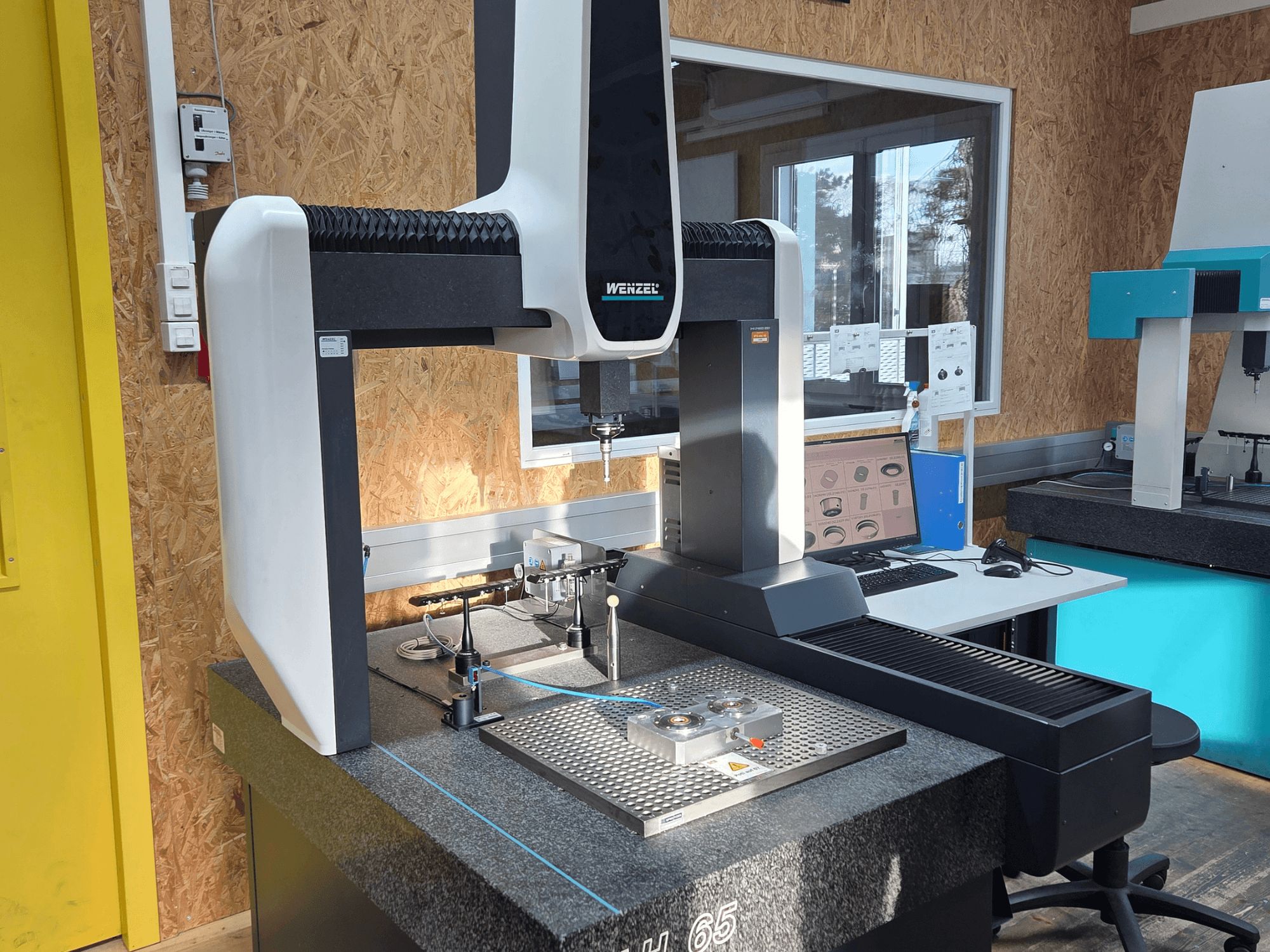 Machine à mesurer tridimensionnelle Wenzel LH 65 dans un laboratoire, vue de face, montrant des outils de mesure et un moniteur.