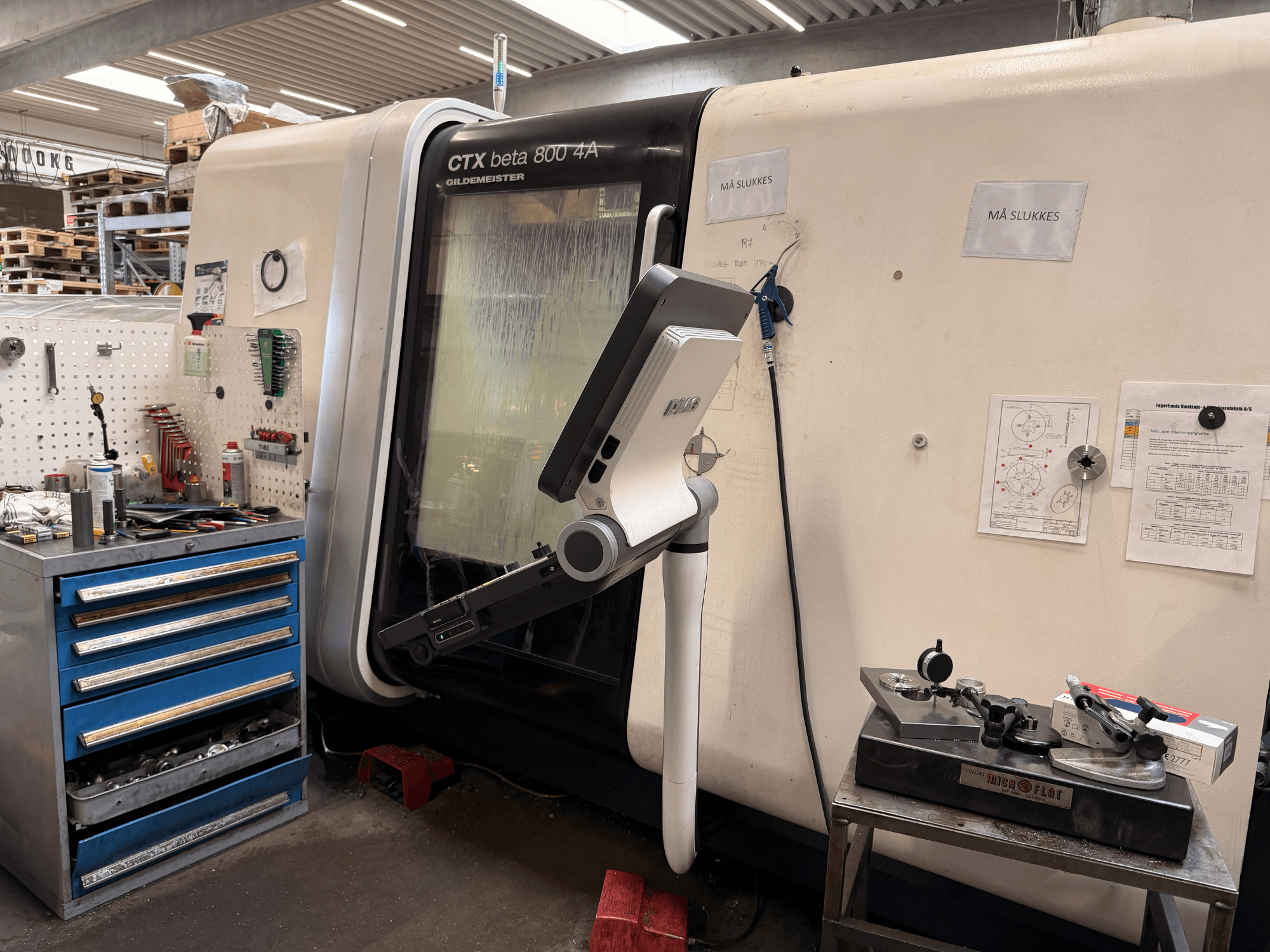 Tour vertical DMG MORI CTX Beta 800 4a dans un atelier, avec un bras de commande et des documents techniques à proximité.