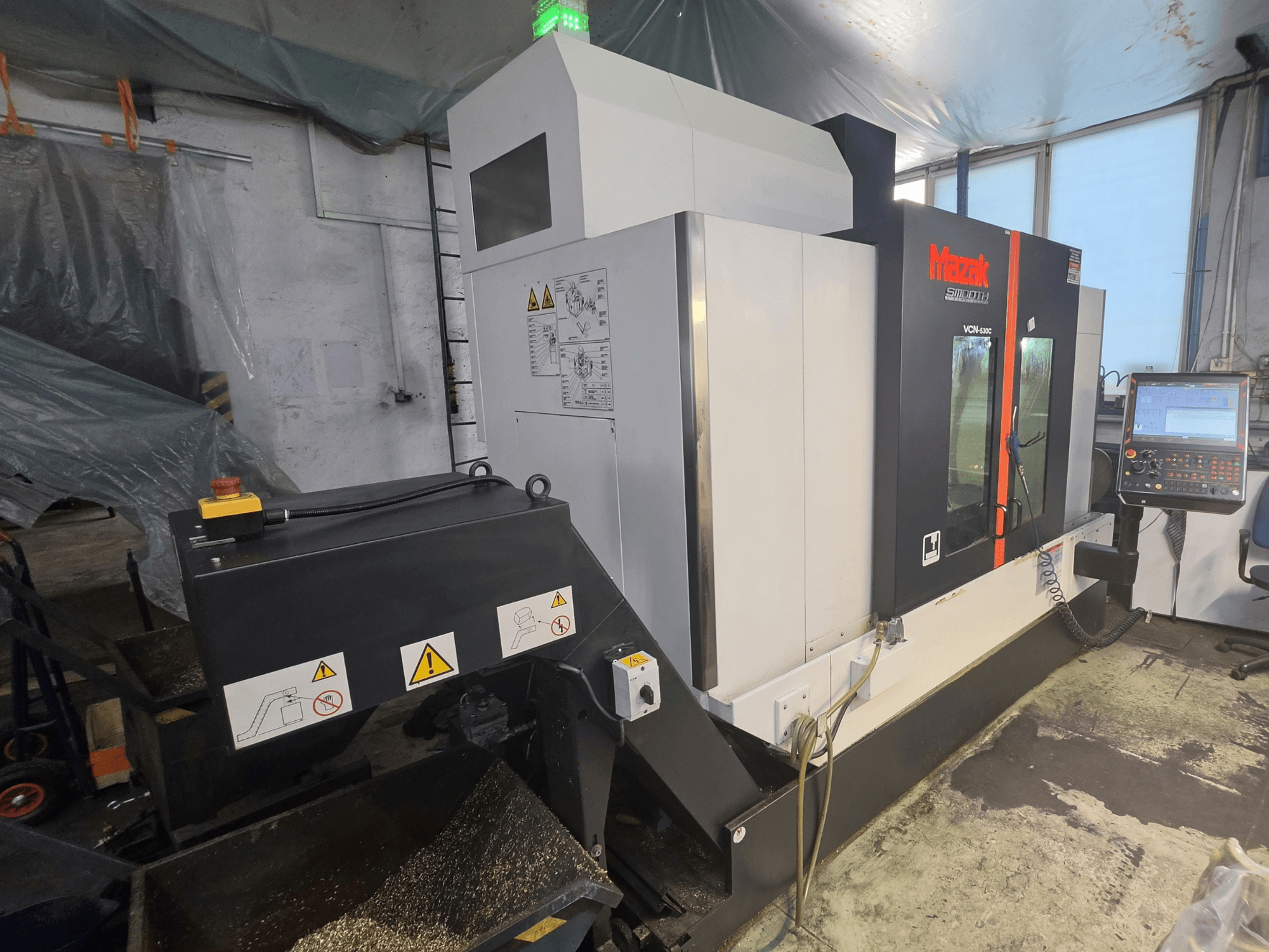 Vue de face du centre d'usinage vertical Mazak VCN-530C, montrant le panneau de commande, la chaîne d'outils et les voyants de fonctionnement.