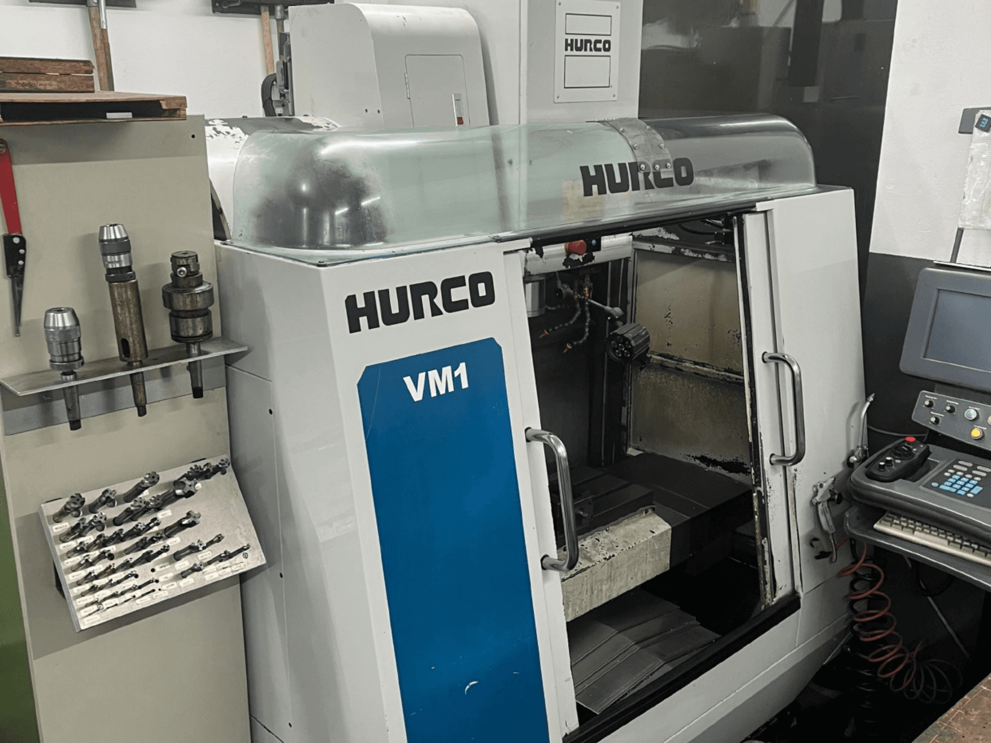 Vue avant du centre d'usinage vertical Hurco VM1, avec un couvercle transparent, un panneau de commande et des outils montés.