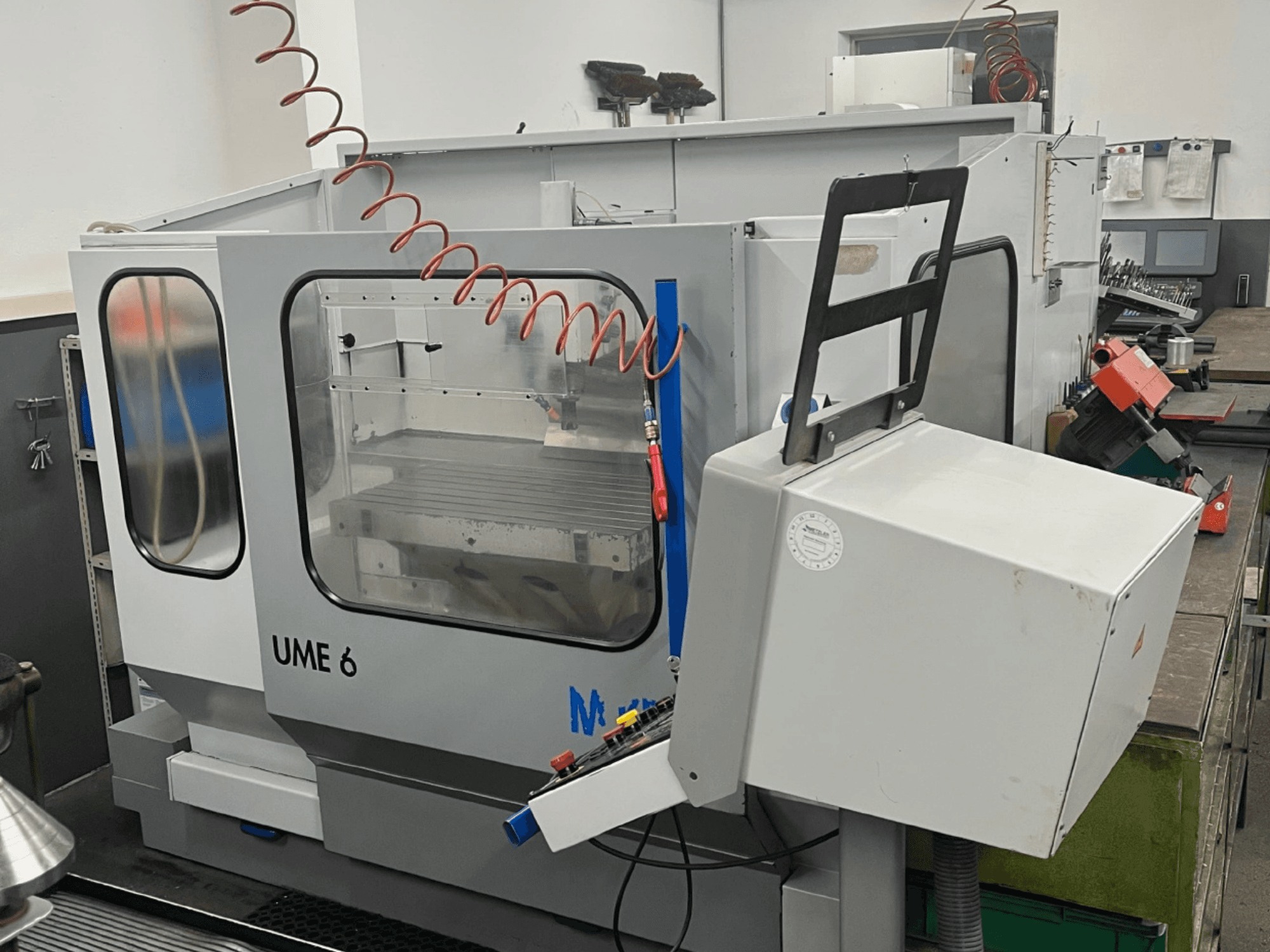Centre d'usinage universel MIKRON UME600 dans un atelier, vue latérale montrant le panneau de commande et le boîtier de protection.