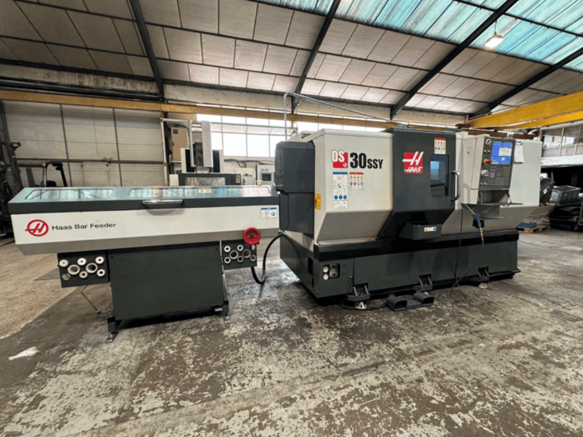 Tour CNC Haas DS-30SSY avec ravitailleur Haas, vue latérale montrant le panneau de commande et le mécanisme d'alimentation dans un atelier.