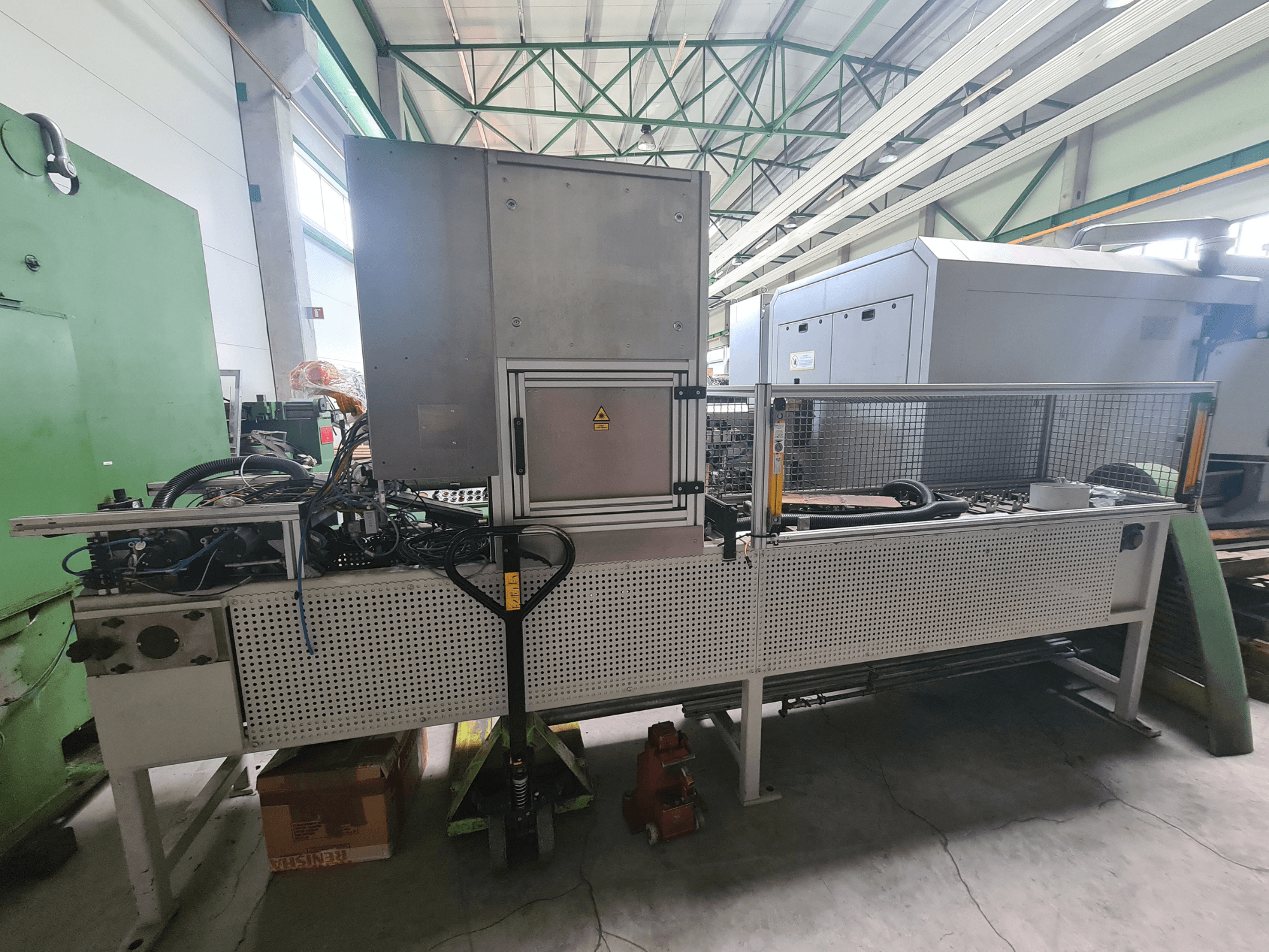 Machine industrielle avec un cadre métallique, des tuyaux et un panneau de commande, vue de côté dans une usine.