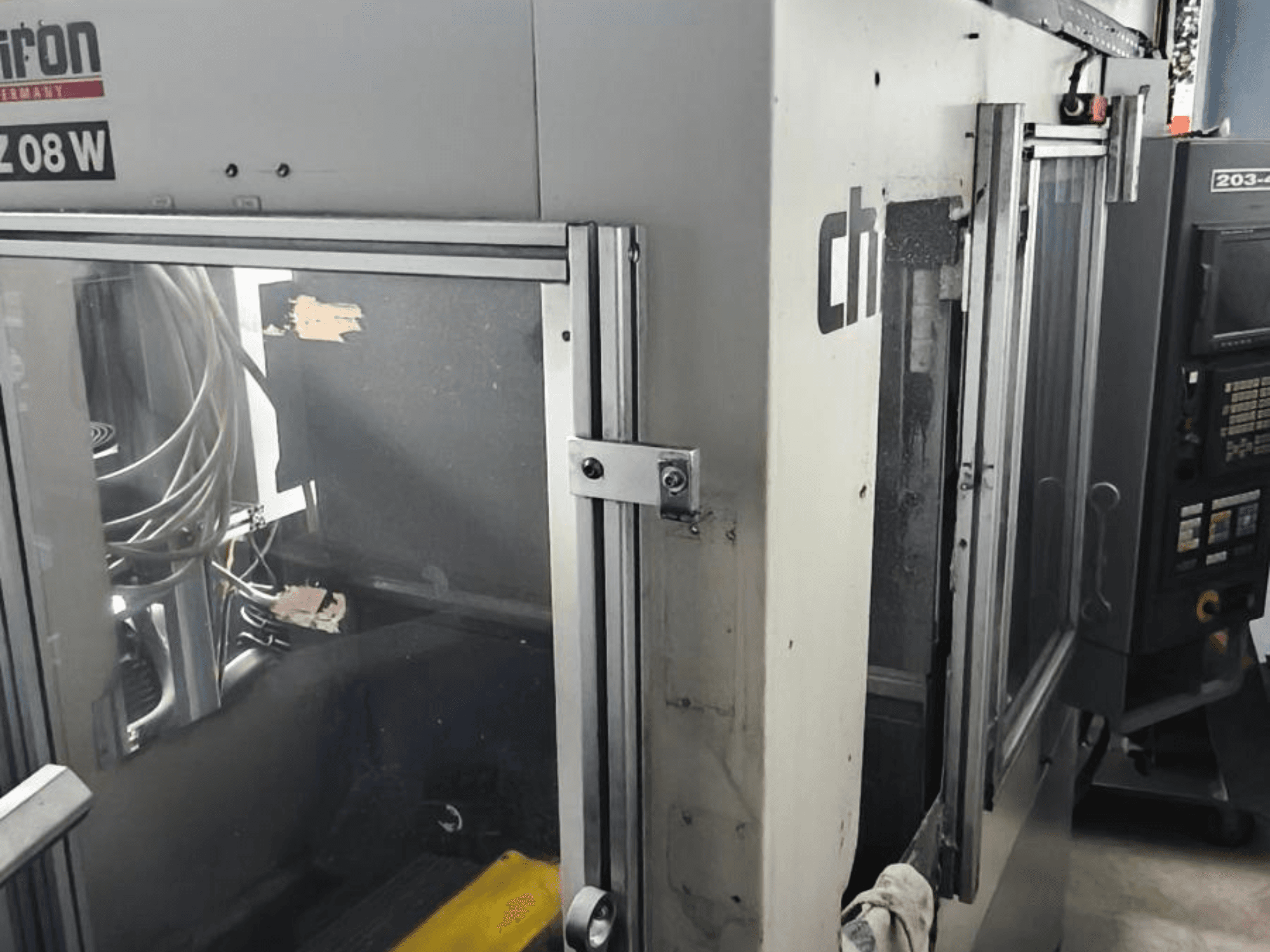 Centre d'usinage vertical CHIRON FZ 08 W, vue de face montrant le panneau de commande et les portes partiellement ouvertes, avec les composants internes visibles.