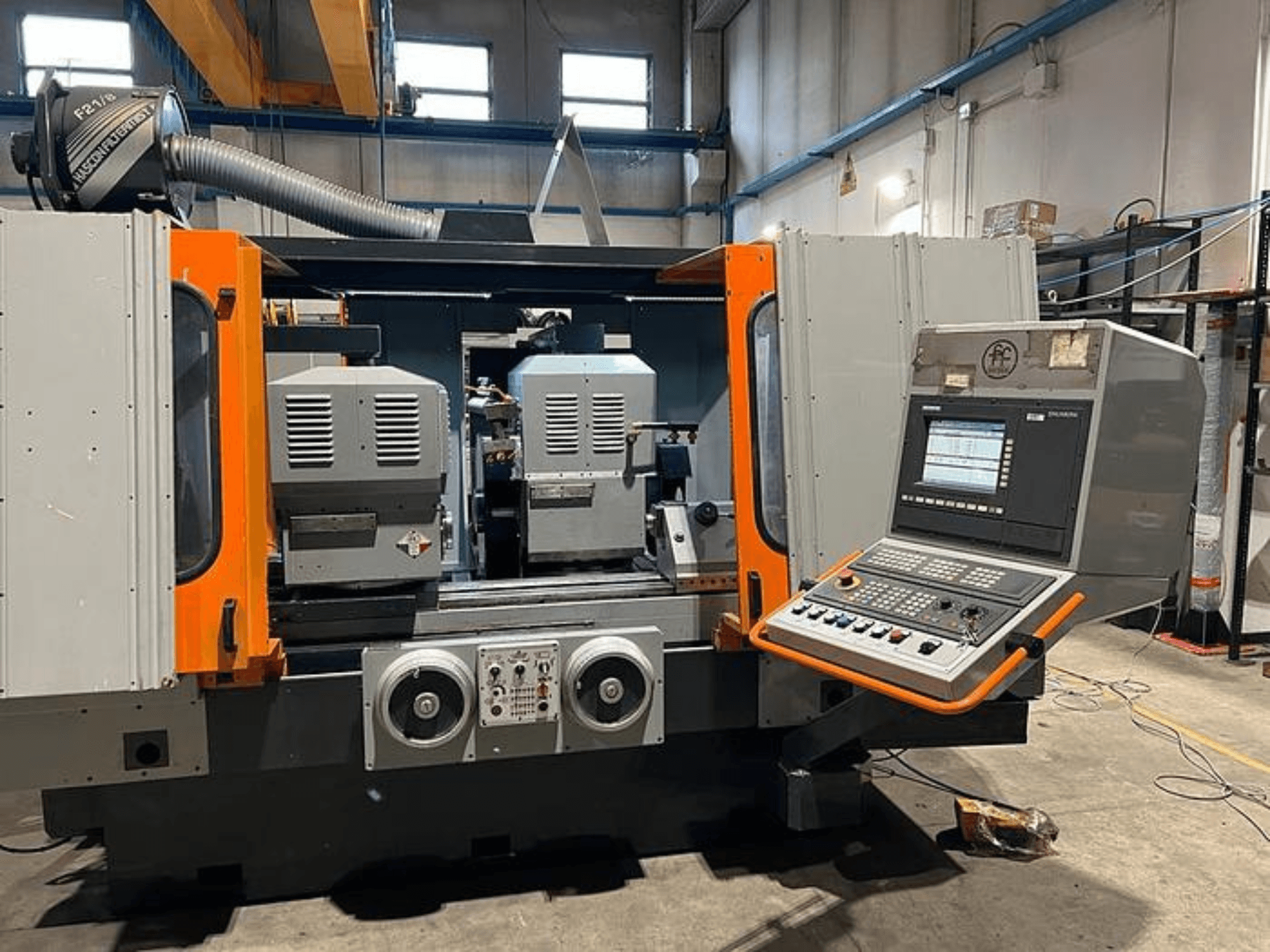 Vue frontale d'une machine CNC avec deux broches, un panneau de commande et des accents orange. Conduit de ventilation et commandes opérationnelles.