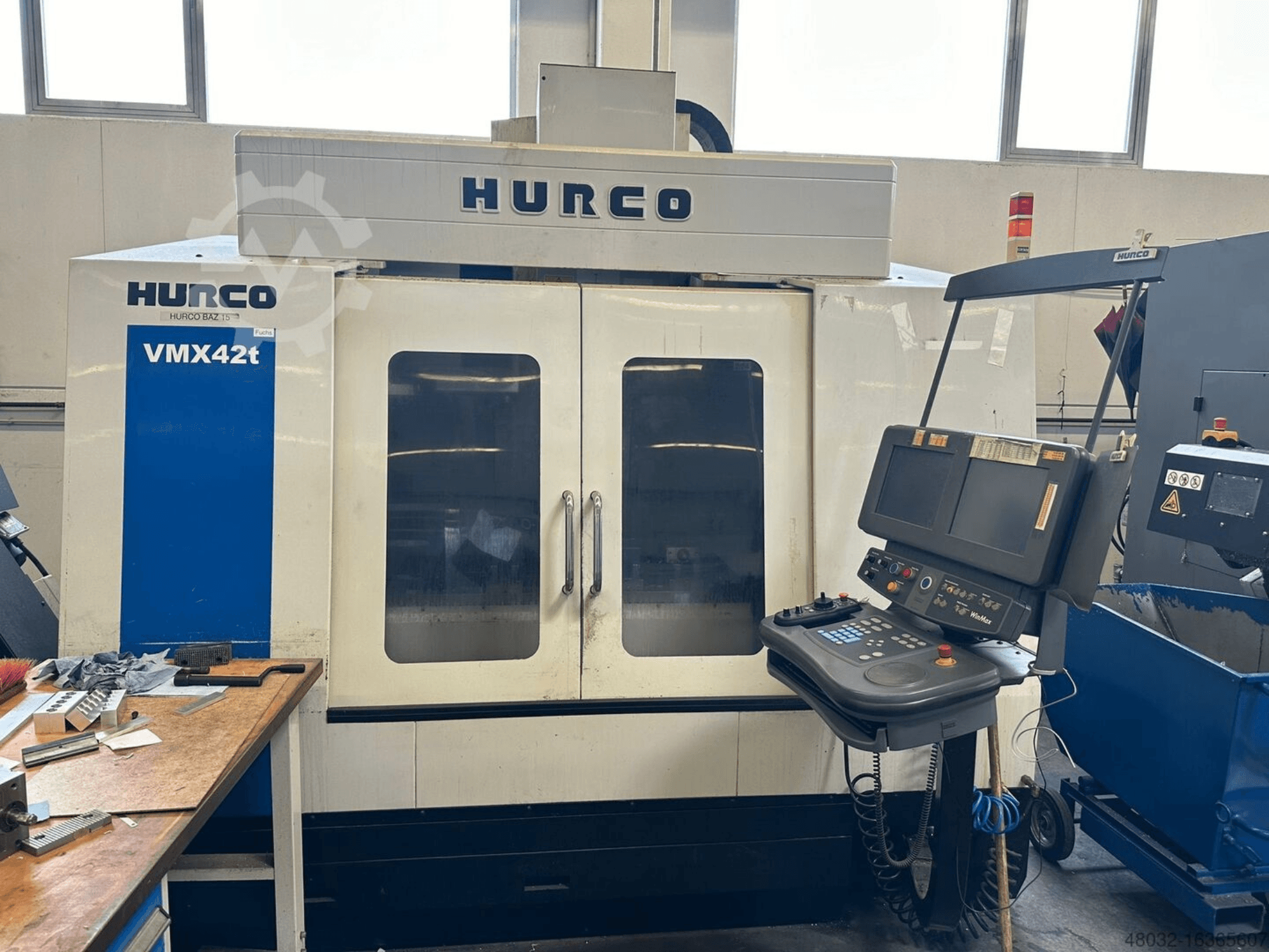 Centre d'usinage vertical Hurco VMX42t, vue de face, montrant le panneau de commande et l'intérieur avec les outils et les pièces à usiner.