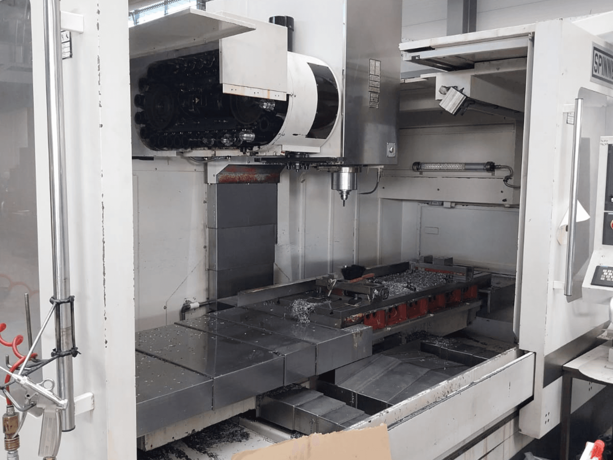 Vue avant du centre d'usinage vertical SPINNER MVC 1600 montrant l'espace de travail ouvert, la broche et les copeaux de métal sur la table.