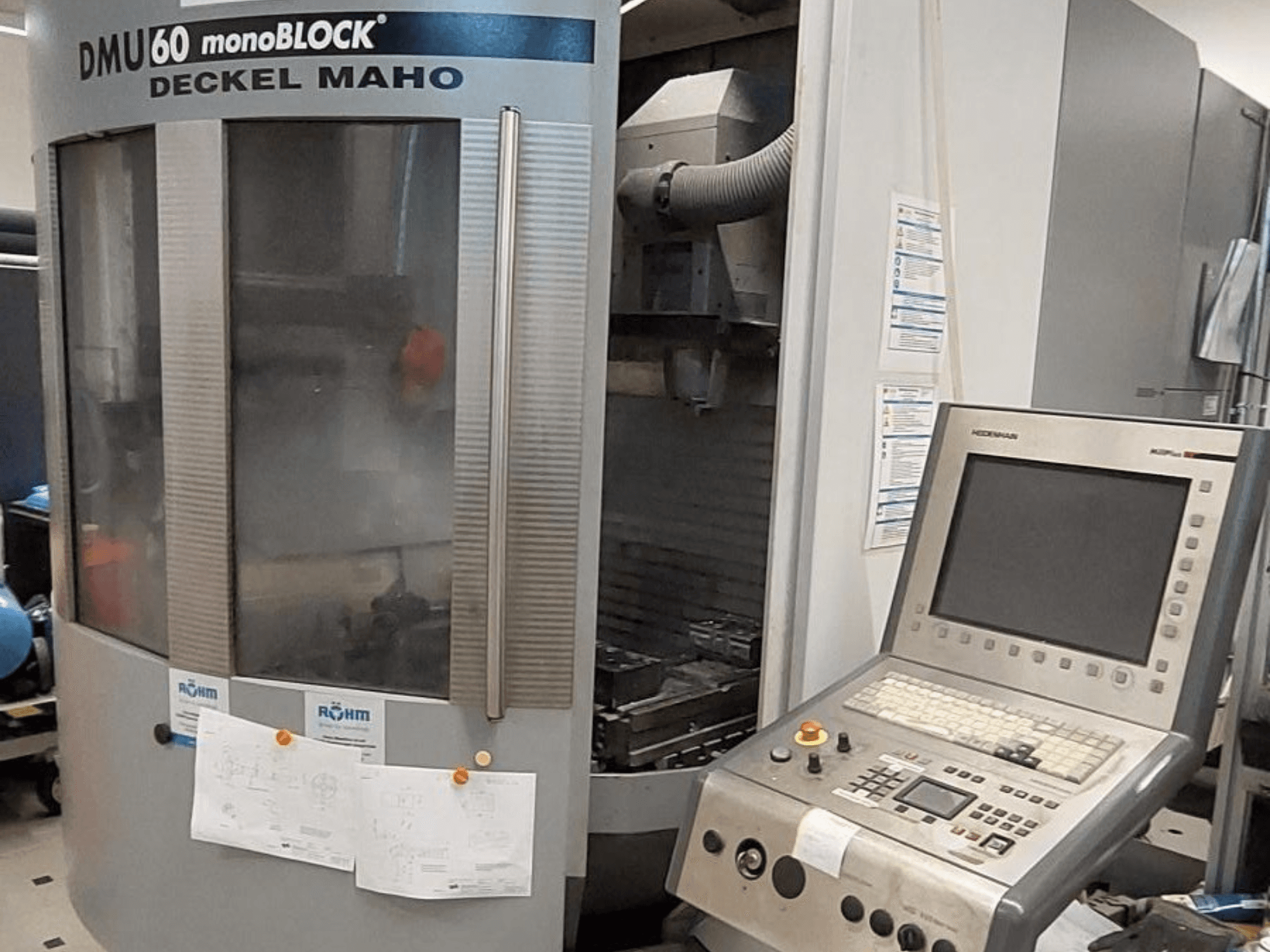 DMU 60 monoBLOCK de Deckel Maho, vue de face d'une fraiseuse CNC avec un panneau de commande et des dessins techniques attachés.