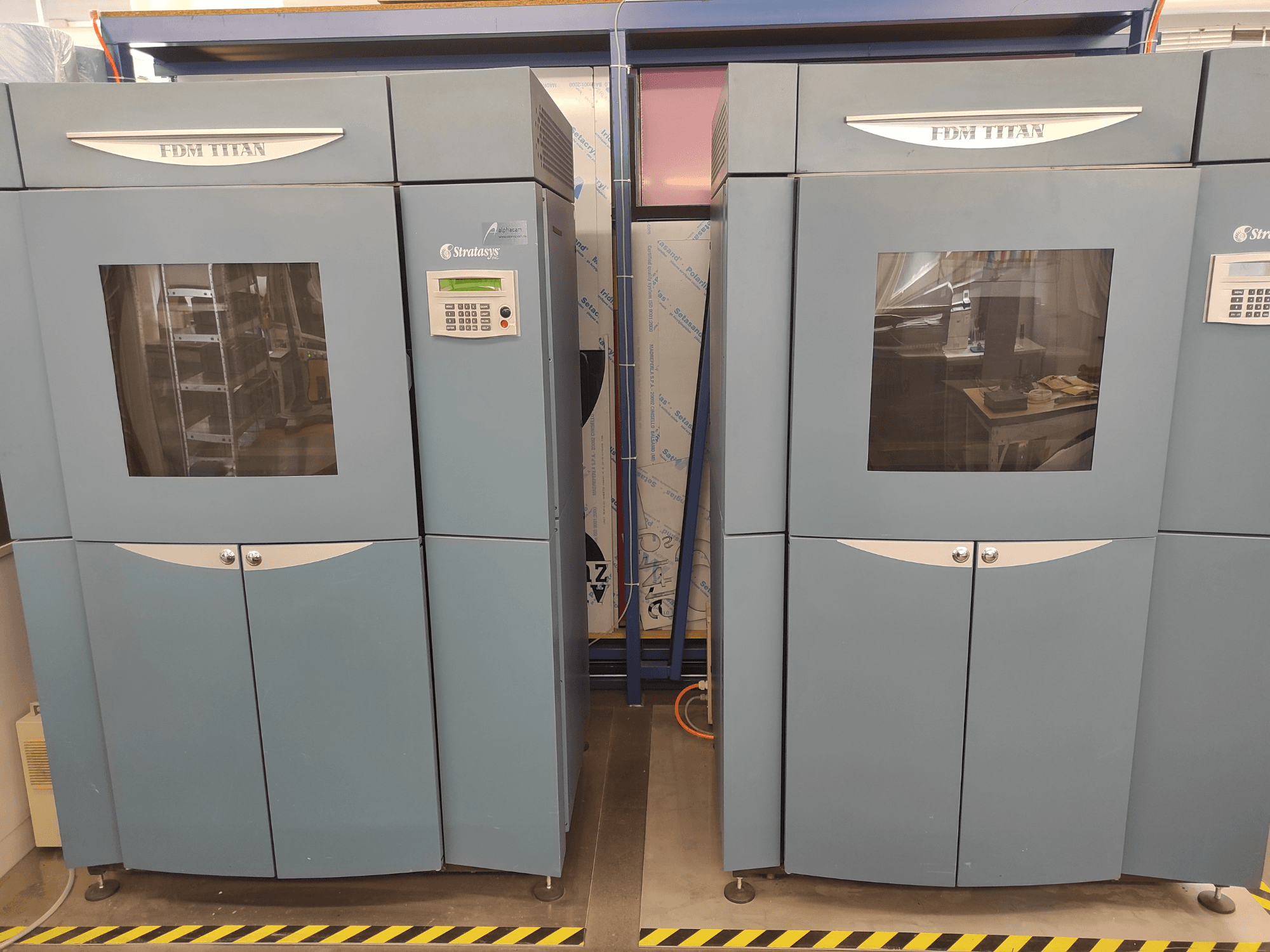 Imprimante 3D FDM TitanTI de Stratasys, vue de face, dotée de deux portes et d'un panneau de commande, installée dans un environnement industriel.