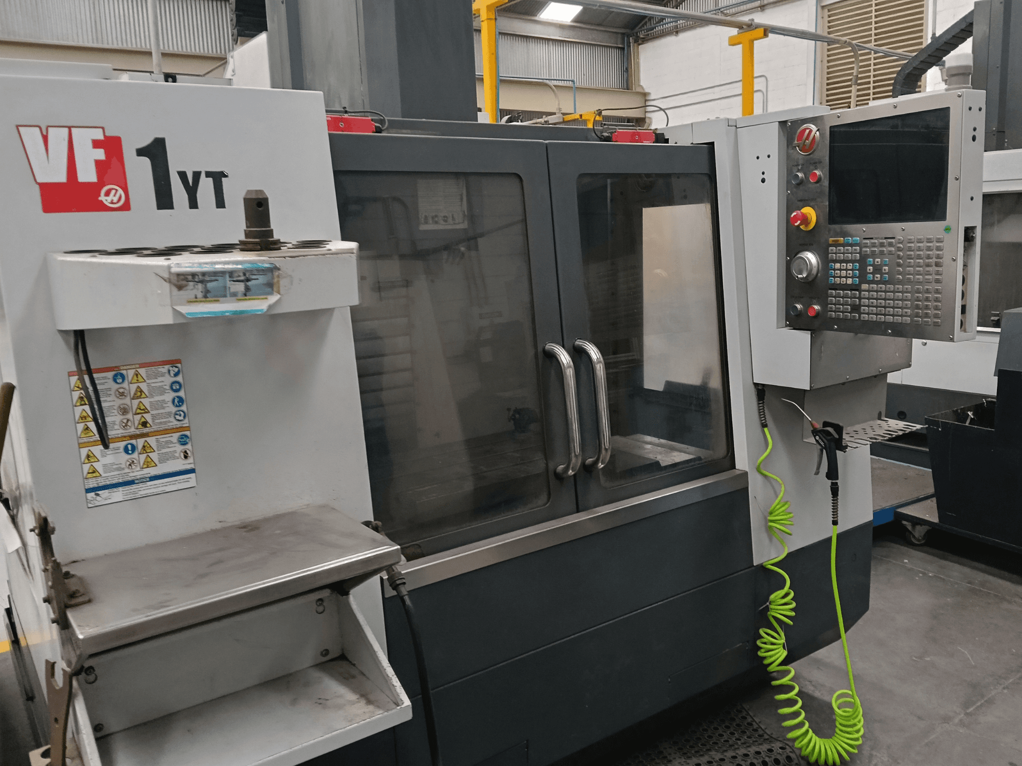 Centre d'usinage vertical HAAS VF-1YT-2, vue de face, montrant le panneau de commande, le porte-outil, les étiquettes de sécurité et la zone d'usinage.