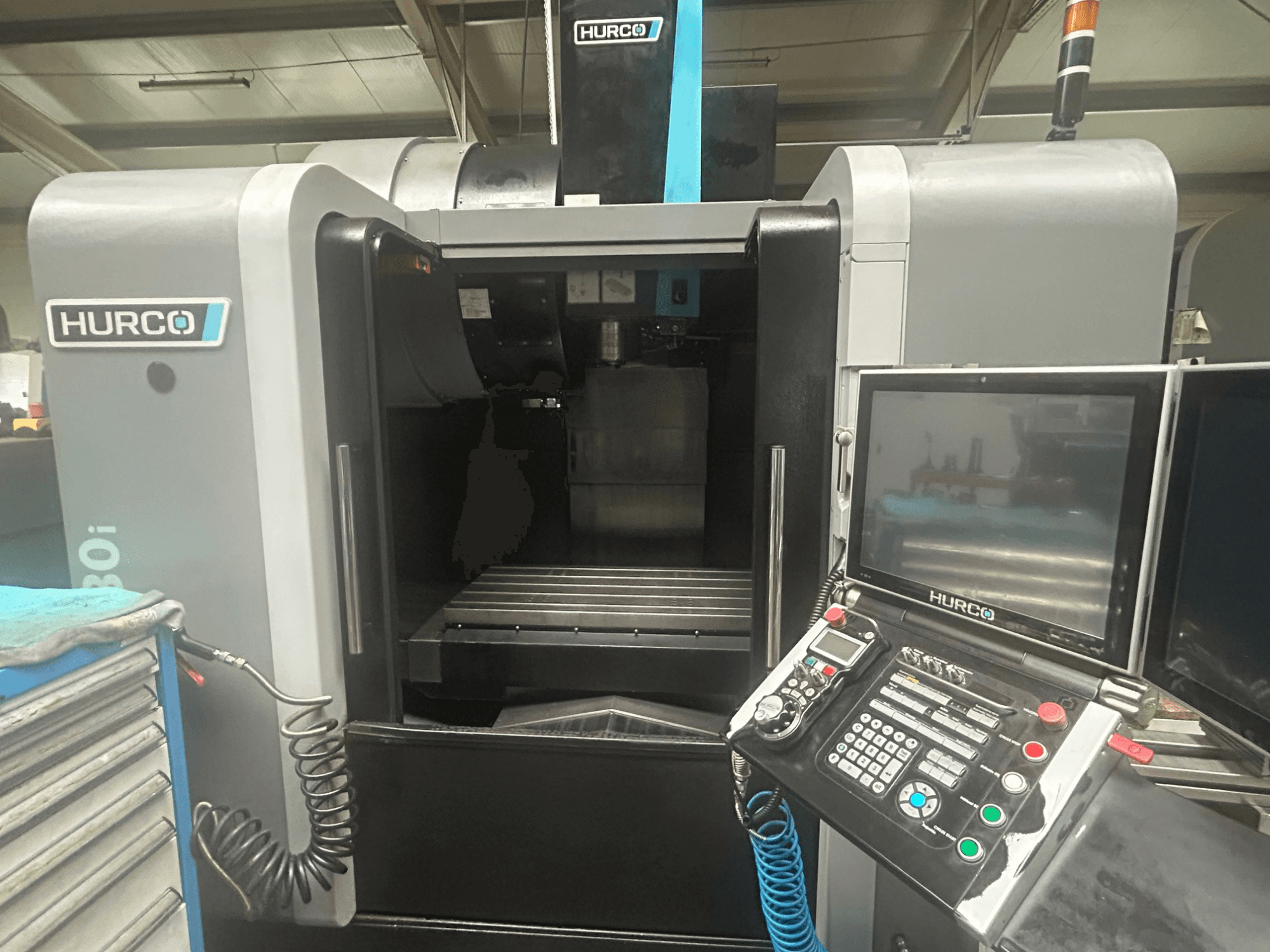 Vue avant de la machine CNC Hurco VM30i, comprenant le panneau de commande avec les boutons, l'écran et la zone de stockage des outils.