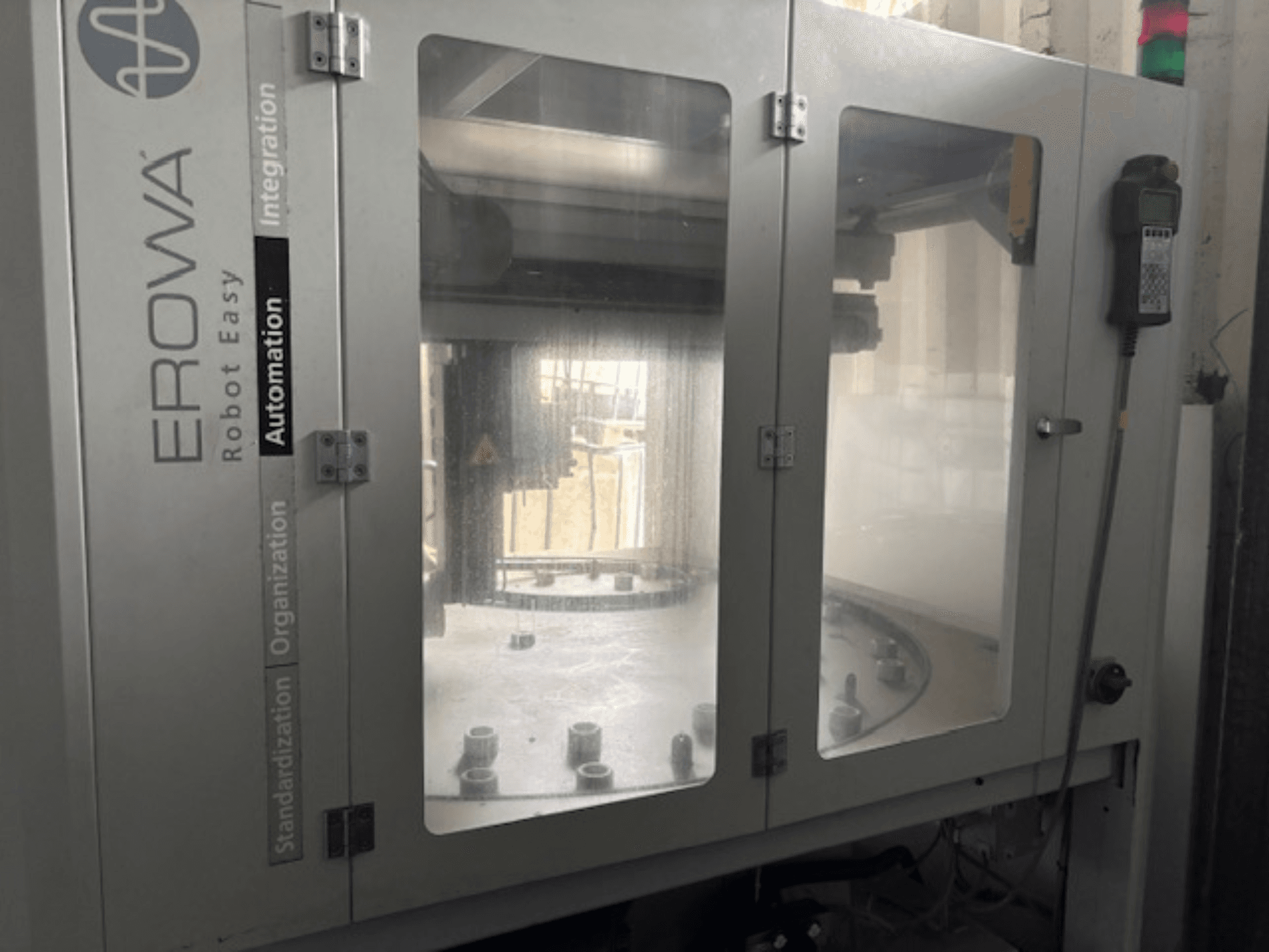 Vue frontale de l'EROWA Robot Easy Automation ; portes transparentes, composants d'automatisation visibles et panneau de commande.