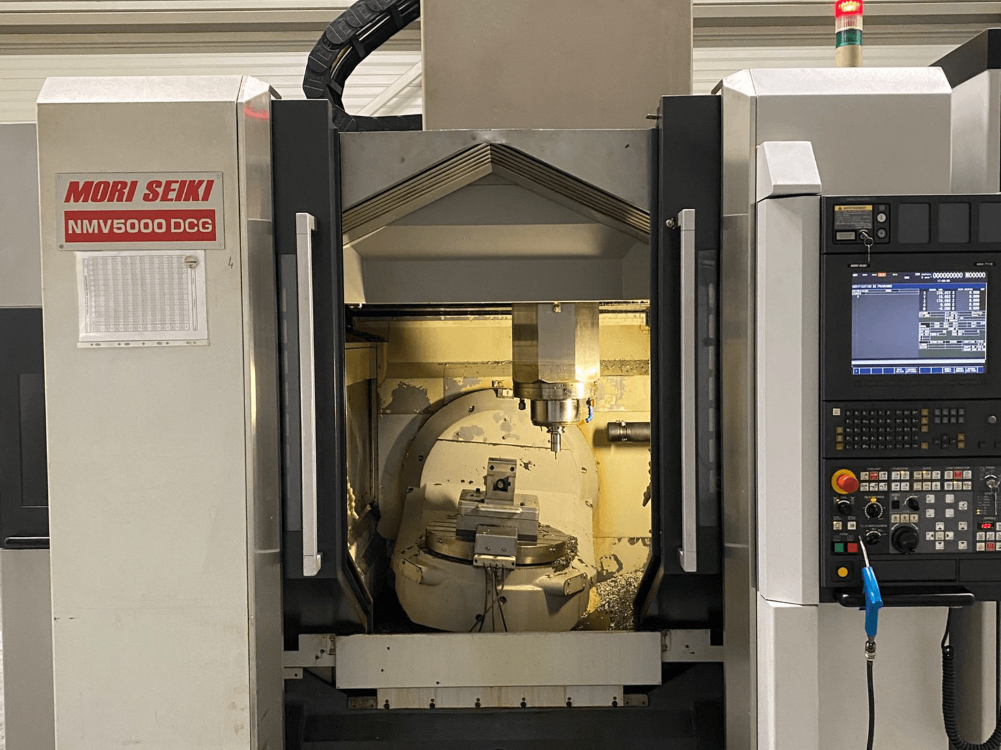 Centre d'usinage universel MORI SEIKI NMV 5000DCG, vue de face montrant le panneau de commande et la zone d'usinage intérieure.