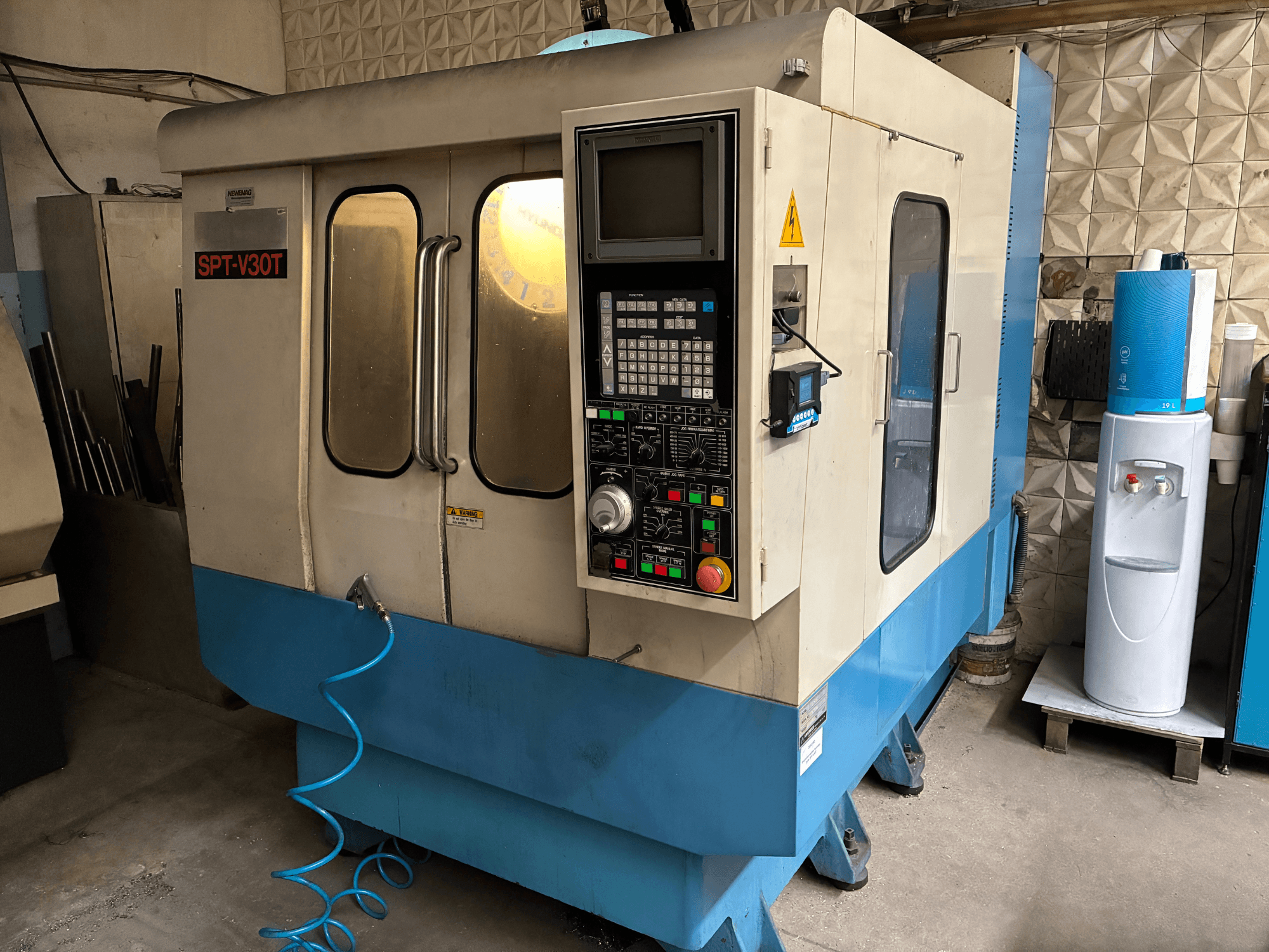 Machine CNC SPT-V30T en bleu et blanc, vue de face montrant le panneau de commande, les portes et le tuyau d'air. Parfaite pour l'usinage de précision.