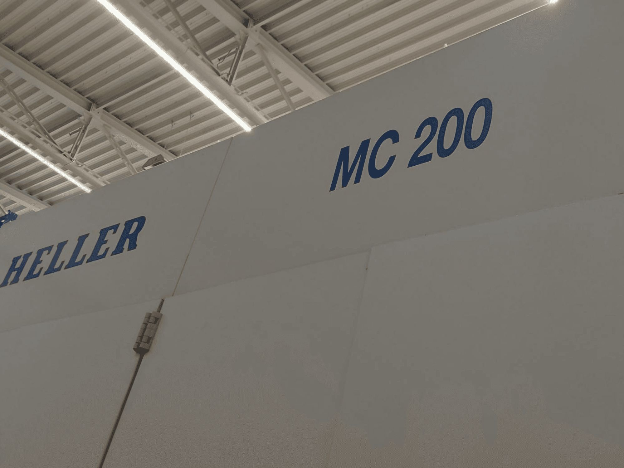 Centre d'usinage horizontal Heller MC 200, présenté de côté, mettant en évidence la marque et le modèle en lettres bleues sur une surface blanche.