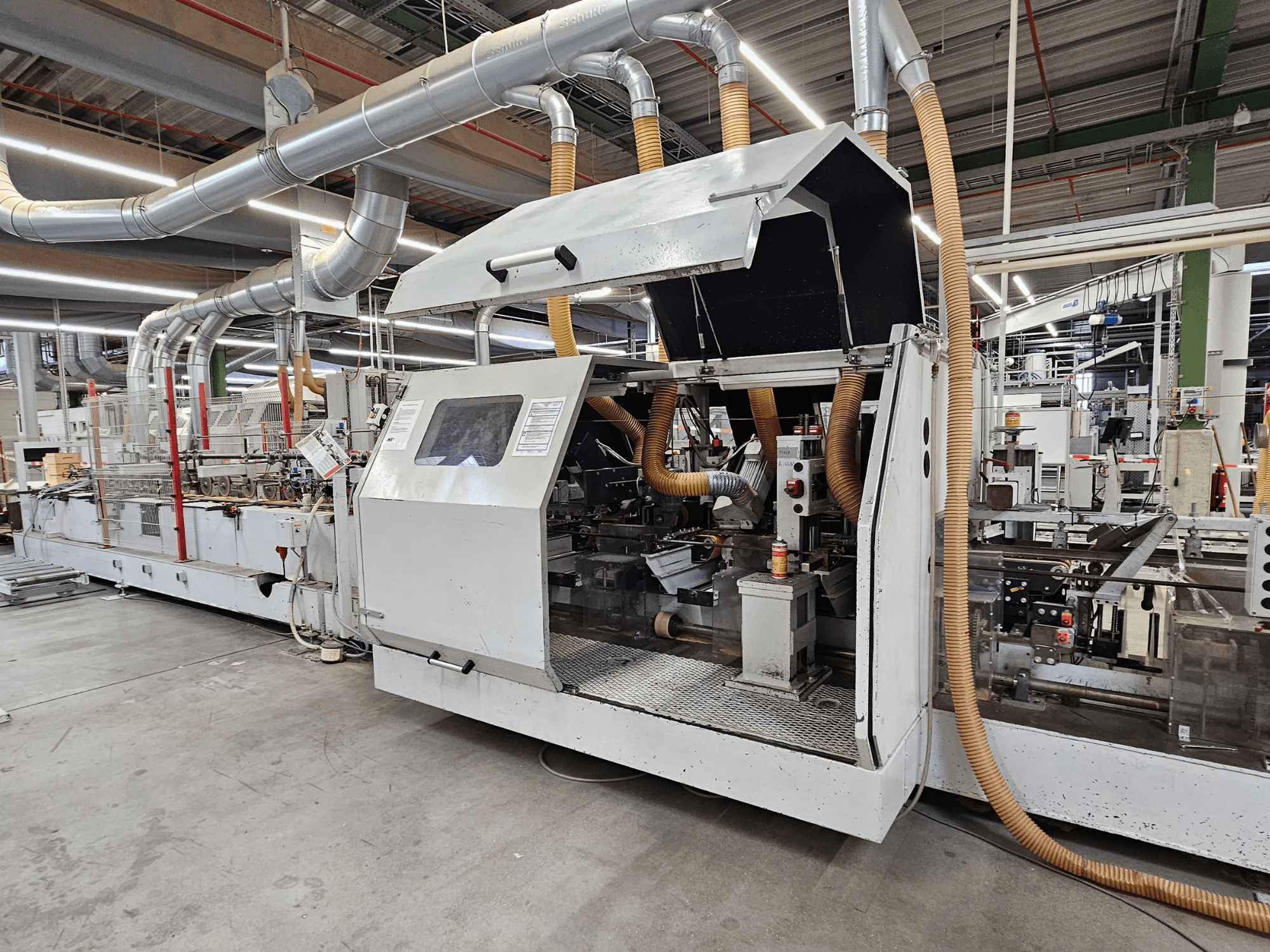 Plaqueuse de chants HOMAG FG63 en usine, vue latérale montrant les composants opérationnels et le système d'extraction des poussières.