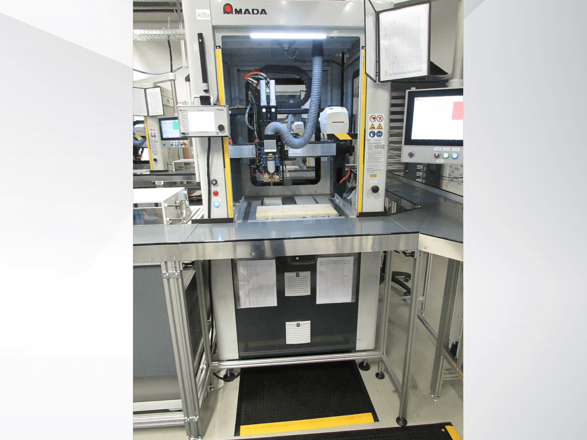 Vue de face de la machine d'automatisation AMADA Jupiter System, avec ses commandes, son écran et un espace de travail dégagé pour l'utilisation.