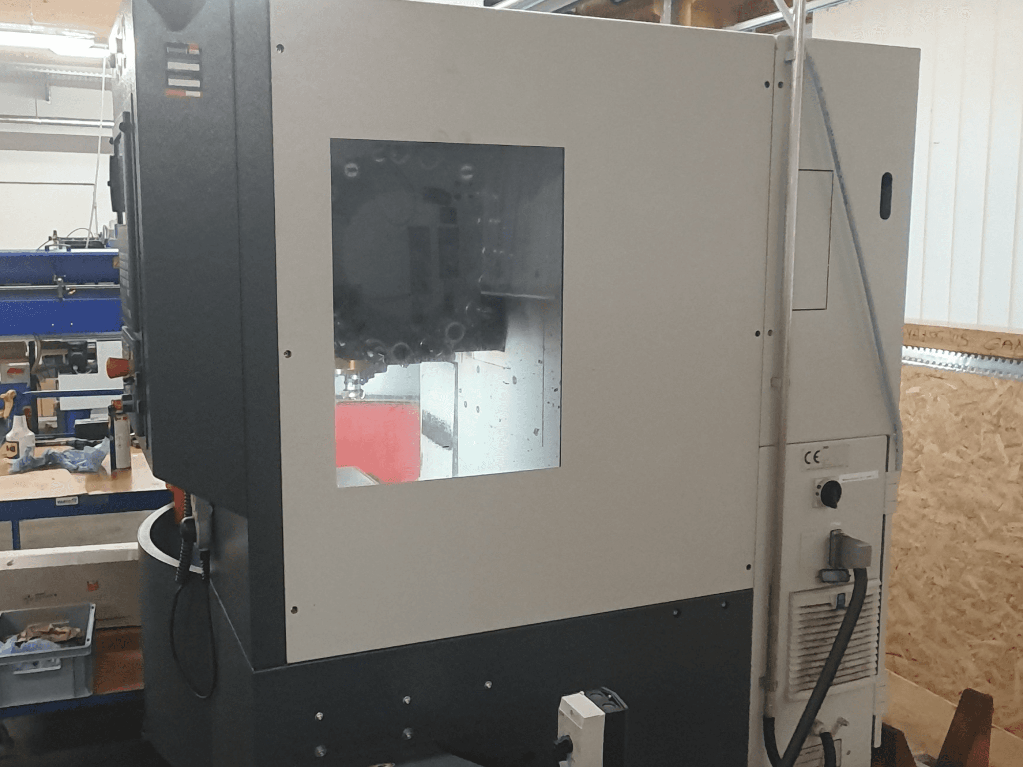 Vue latérale d'une machine à travailler les métaux avec un panneau de commande visible, une grande fenêtre de visualisation et des composants internes complexes.