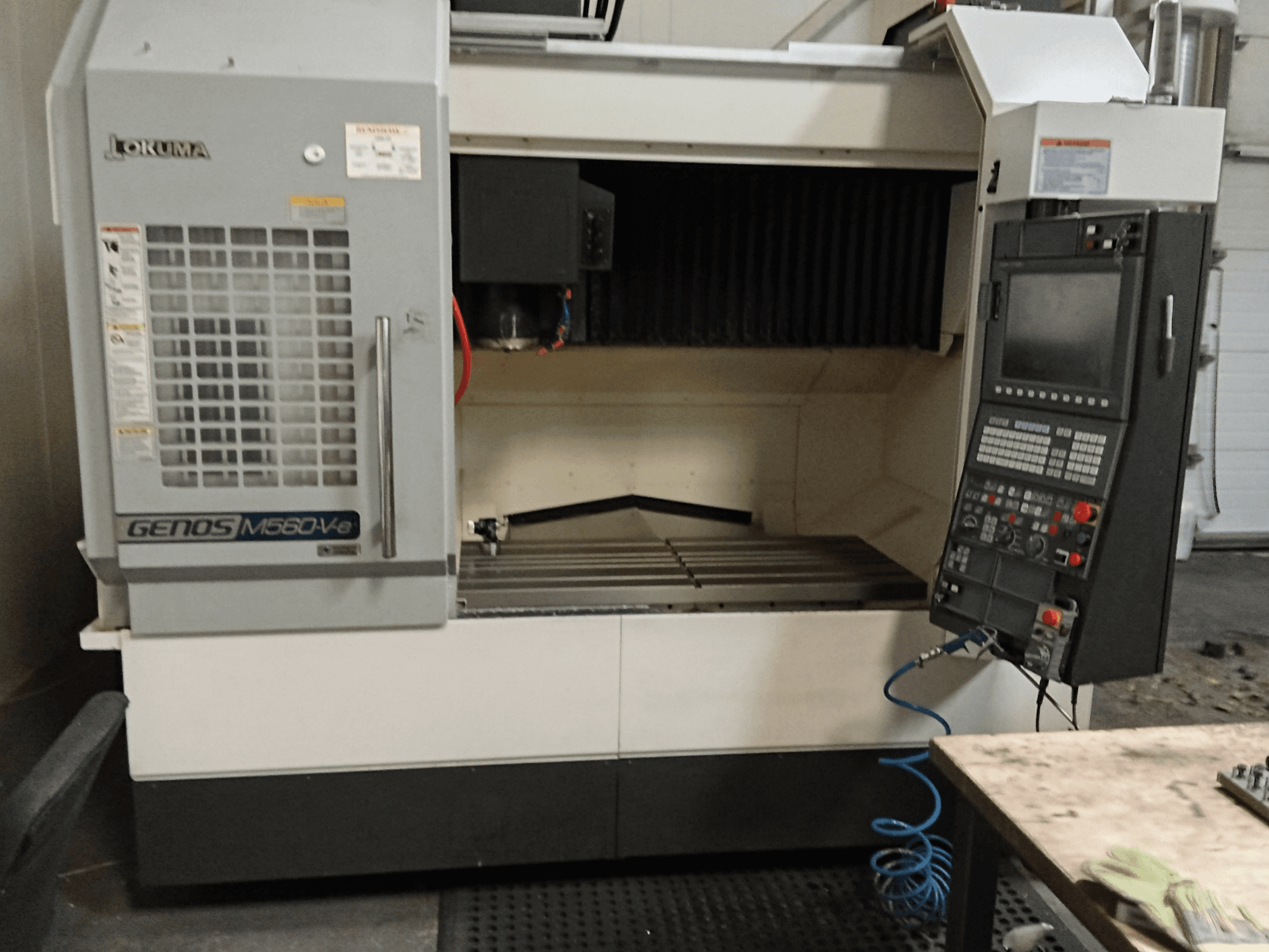 Okuma GENOS M560-V, vue de face d'un centre d'usinage vertical avec panneau de commande, interface CNC et zone de coupe visible.