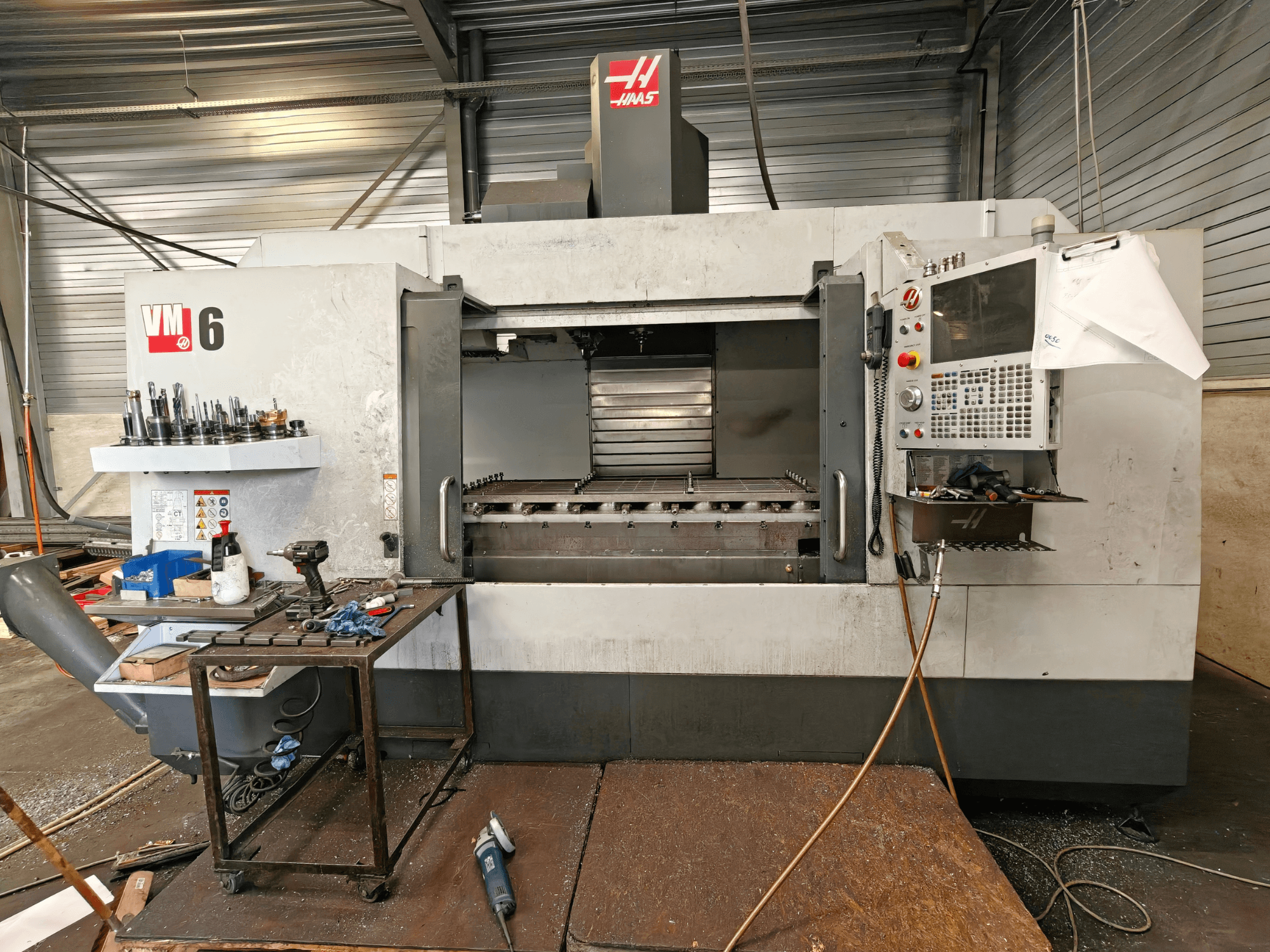 Centre d'usinage vertical Haas VM-6, vue de face, avec le magasin d'outils, le panneau de commande et les débris présents dans la zone de travail.