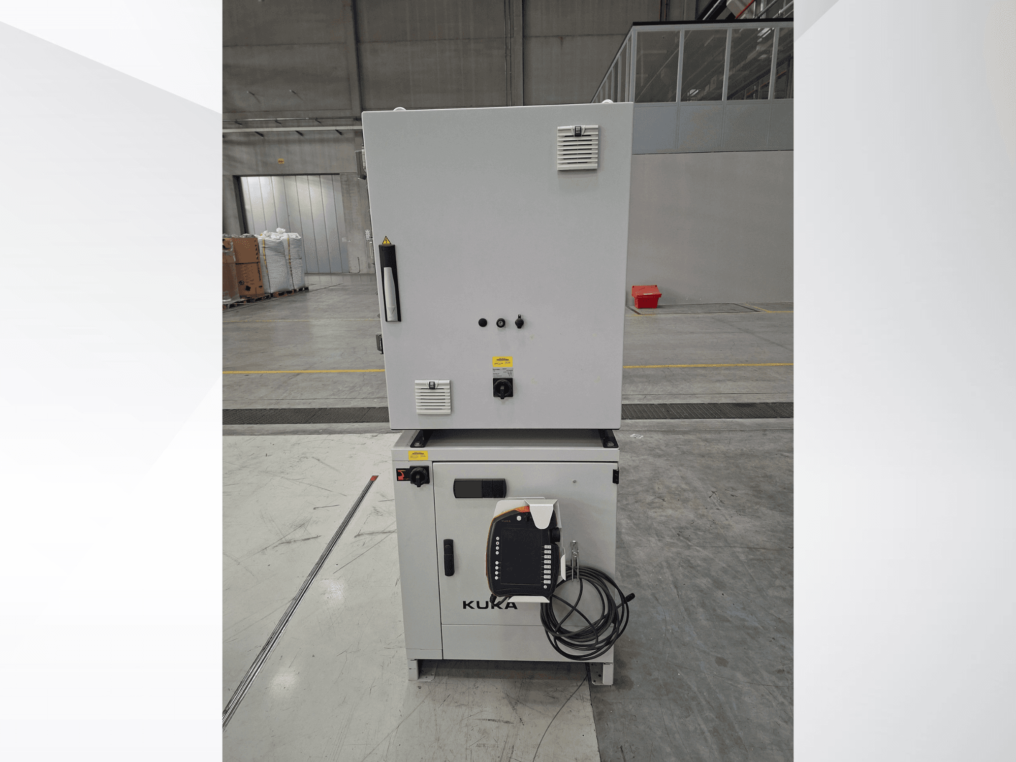 Contrôleur du bras robotisé KUKA KR 90 R2700 PRO C4 FLR, vue de face montrant le panneau de commande et les étiquettes de sécurité dans un entrepôt spacieux.