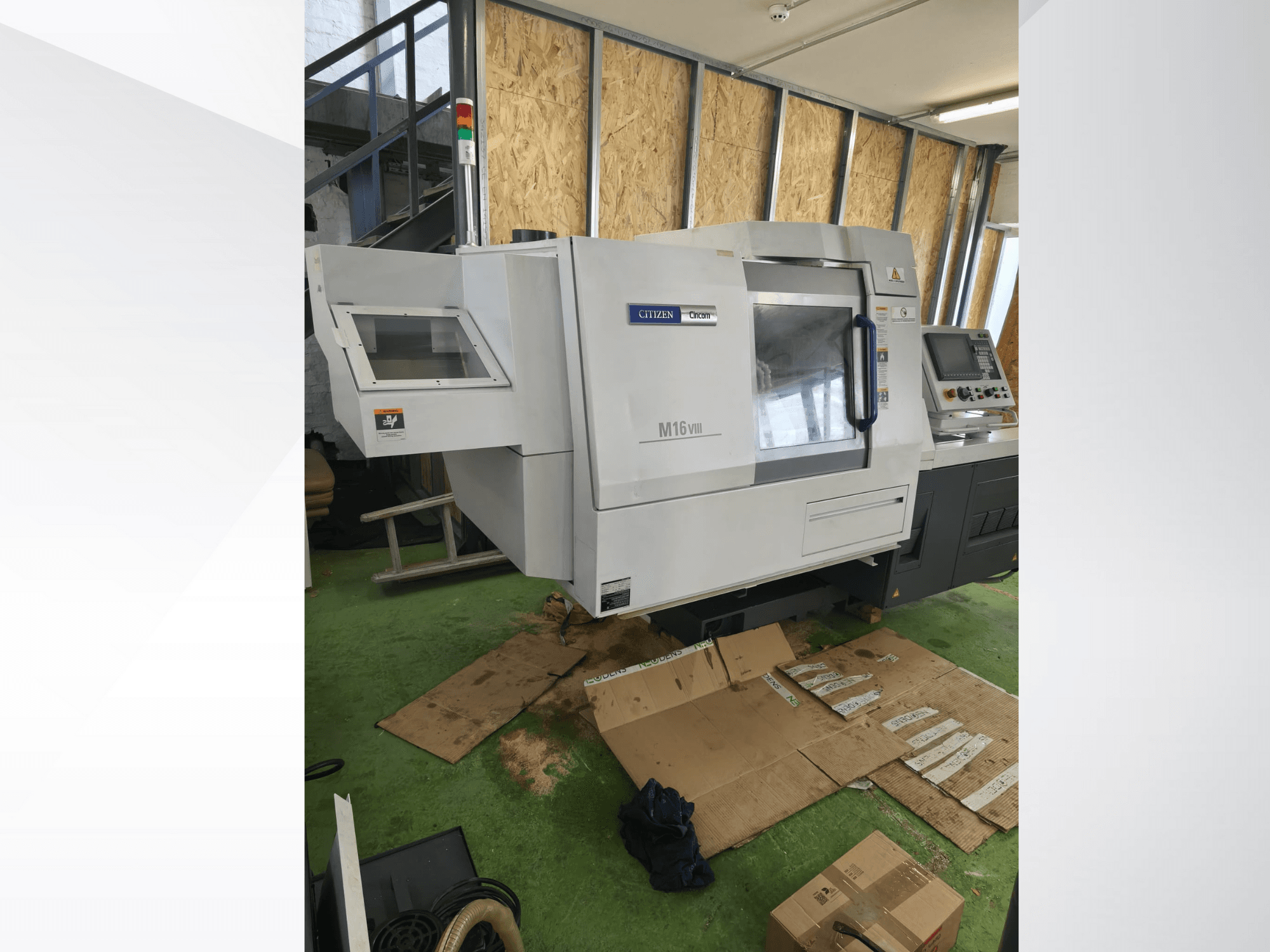 Tour CNC Citizen M16VIII vu de face, doté d'un panneau de commande et de voyants d'alerte de sécurité, placé sur un sol vert.