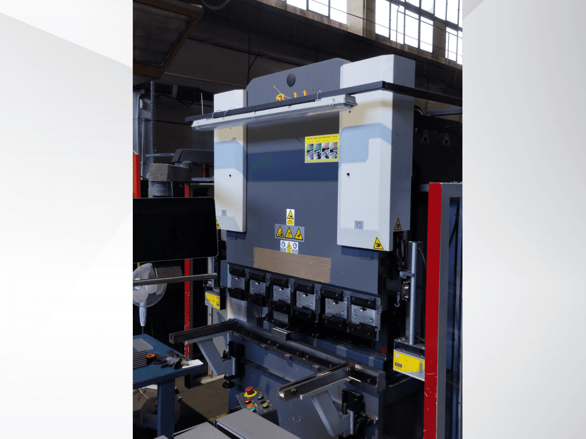 Machine à plier, vue de face. Comprend des commandes visibles, des autocollants de sécurité et plusieurs porte-matrices pour un pliage de précision.