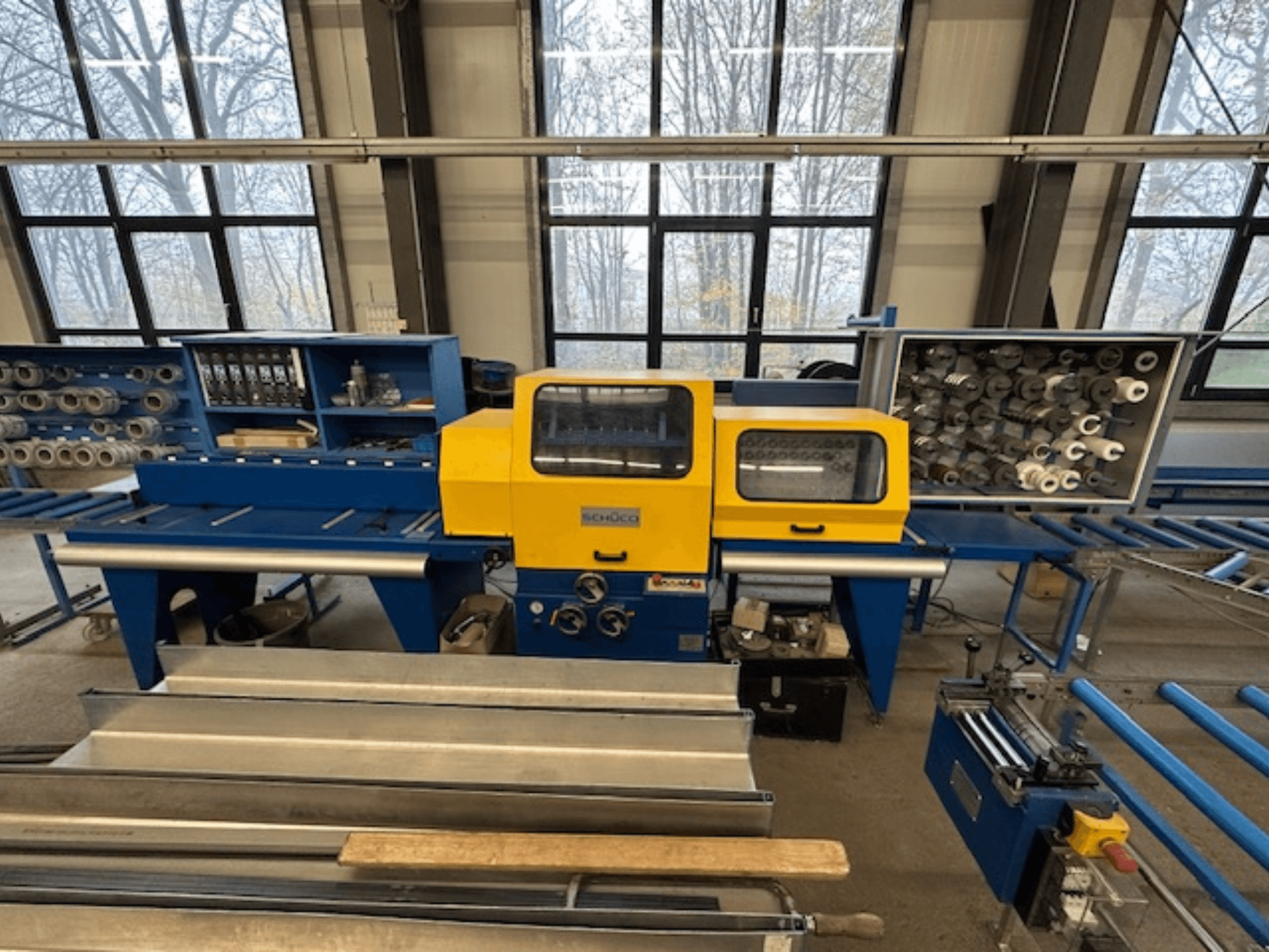 Vue avant de la machine-outil SCHÜCO ISOMAT 4, dotée d'un panneau de commande jaune, de plusieurs rouleaux et d'un compartiment de stockage.