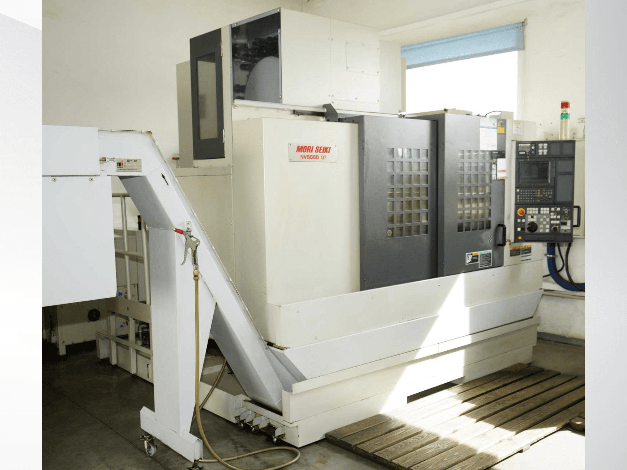 Centre d'usinage vertical MORI SEIKI NV 5000 alpha1 vu de face, mettant en évidence le panneau de commande, les dispositifs de sécurité et la zone de chargement.