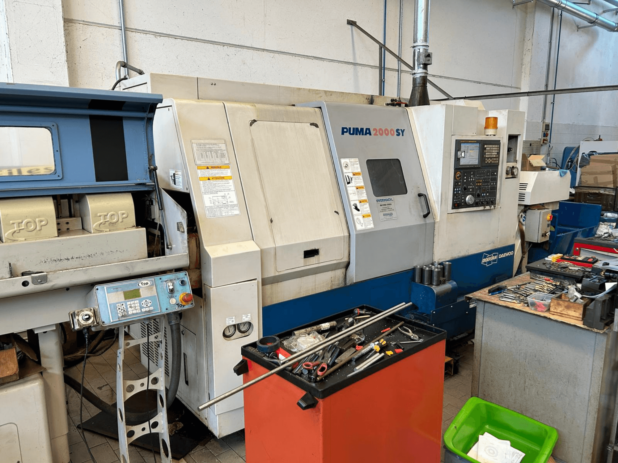 Tour horizontal DOOSAN PUMA 2000SY dans un atelier, vue de profil montrant le panneau de commande et les outils à proximité.