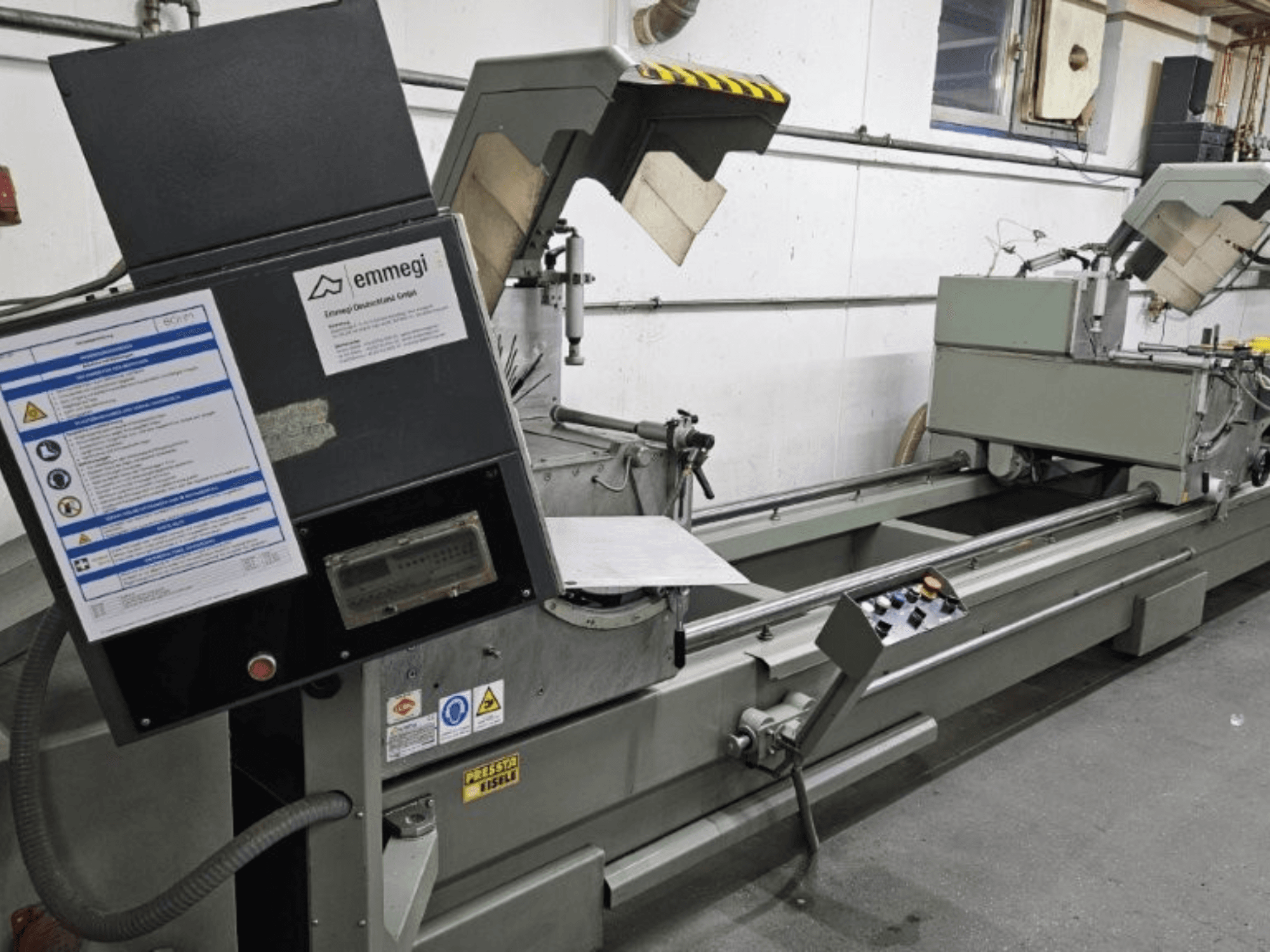 Machine à découper industrielle Emmegi, vue de face, comprenant le panneau de commande, les étiquettes de sécurité et les composants opérationnels.