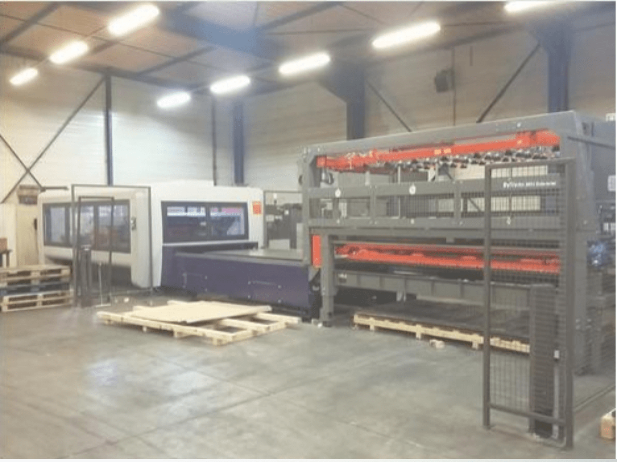 Installation de machines industrielles dans un entrepôt ; comprend une découpeuse laser grise et une défonceuse CNC violette, vue de face avec des palettes.