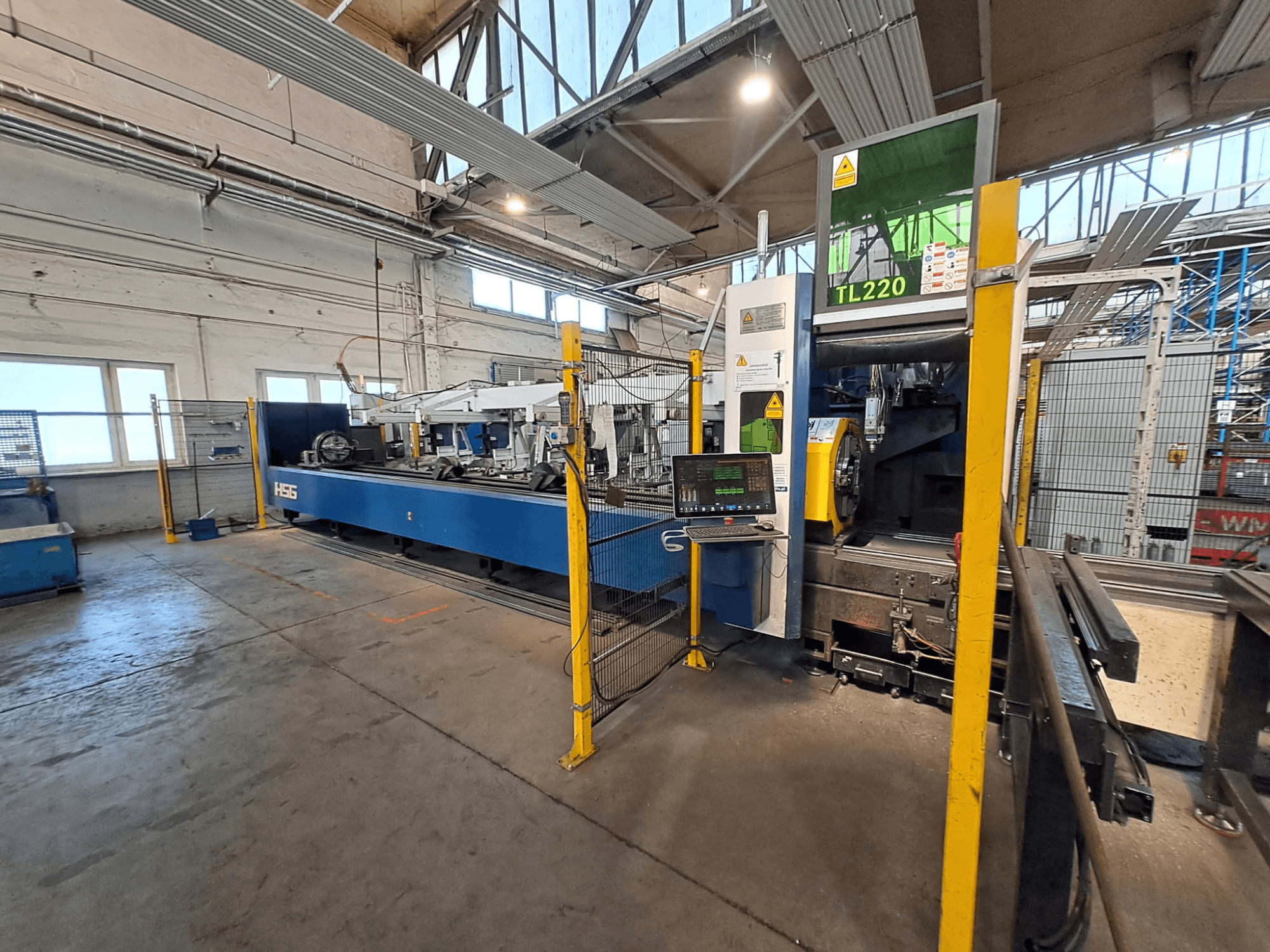 Vue de face de la machine à couper les tubes HSG HS-TL220, avec son panneau de commande et ses barrières de sécurité, dans un environnement industriel.