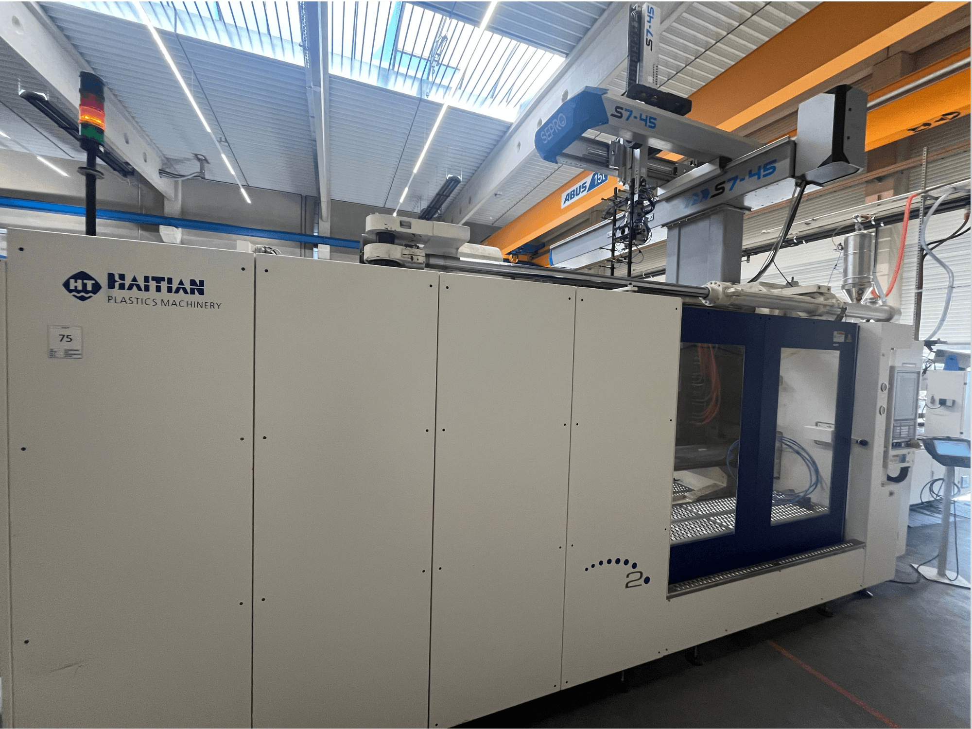 Machine de moulage par injection haïtienne S7-45 vue de côté avec panneau de commande et indicateur lumineux de sécurité. Design blanc et bleu.
