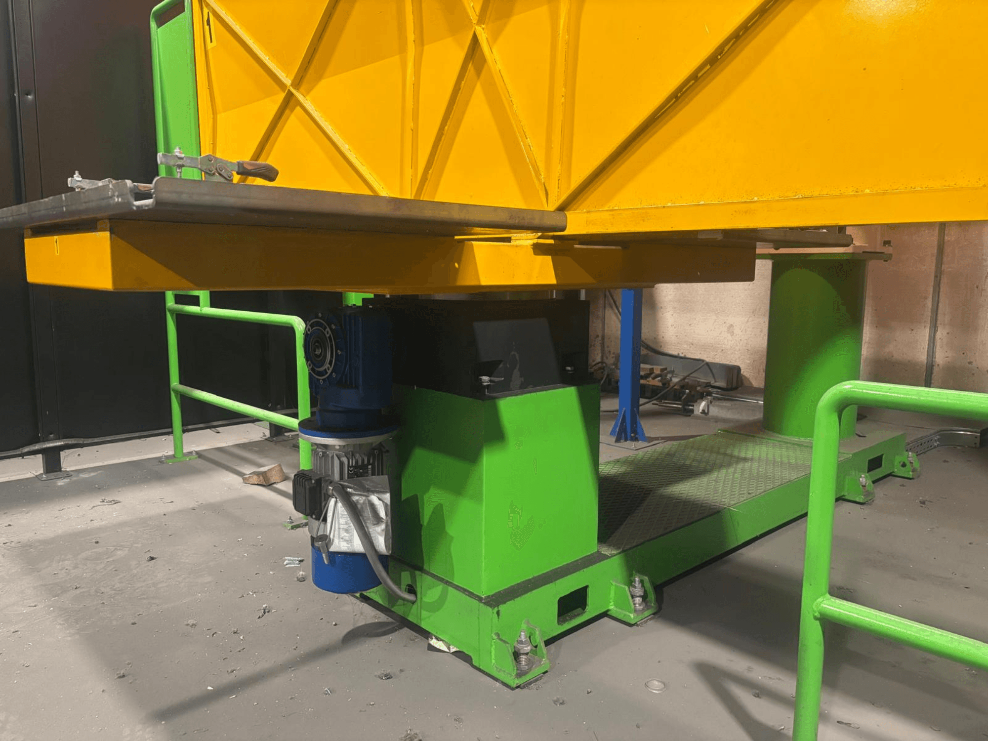 Machines industrielles vertes et jaunes vues de face, comprenant un moteur et une plate-forme à la surface texturée.