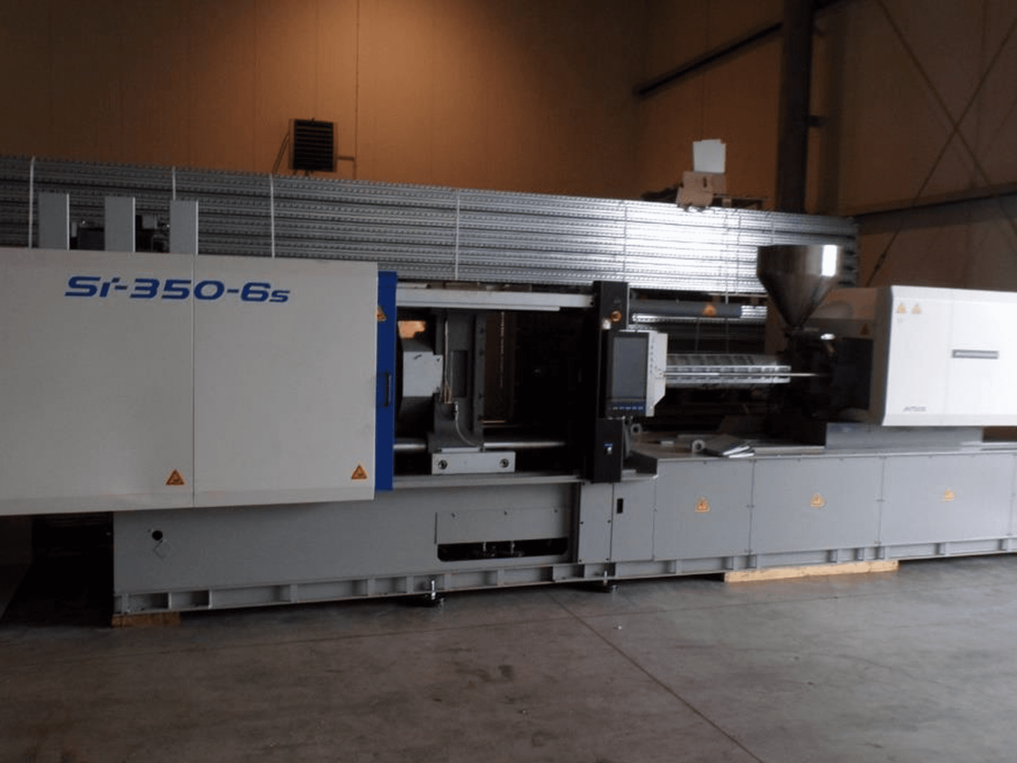 Machine de moulage par injection Si-350-6s vue de côté, comprenant une trémie et un panneau de commande, située dans un environnement industriel spacieux.