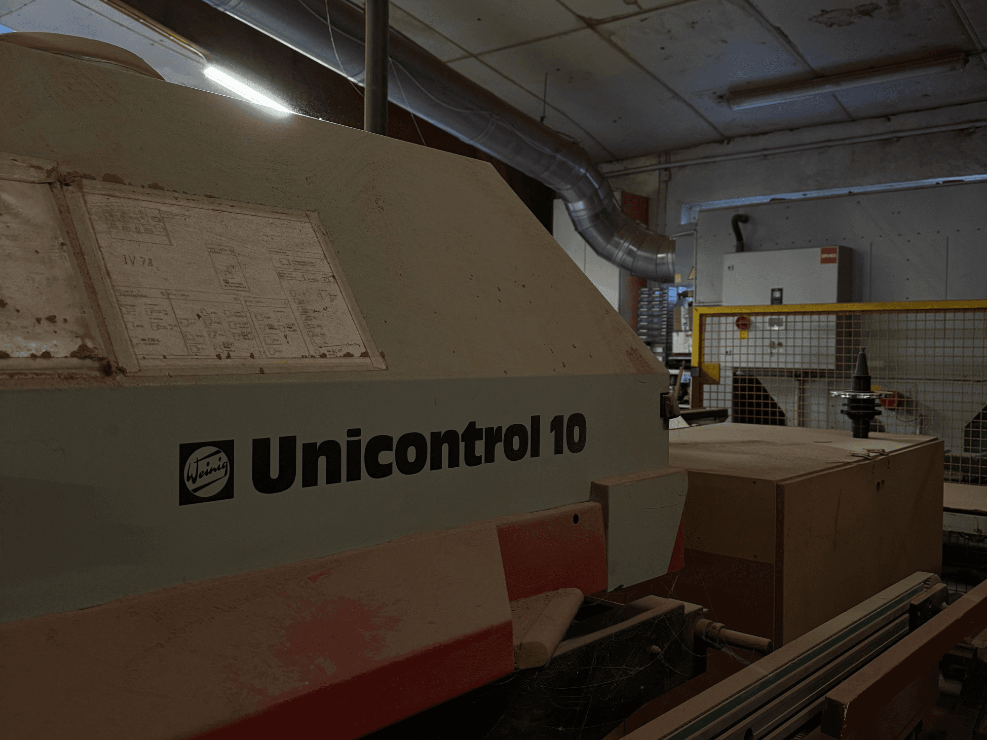 Machine Weinig Unicontrol 10 vue de côté, surface poussiéreuse, schémas techniques visibles sur la face avant.