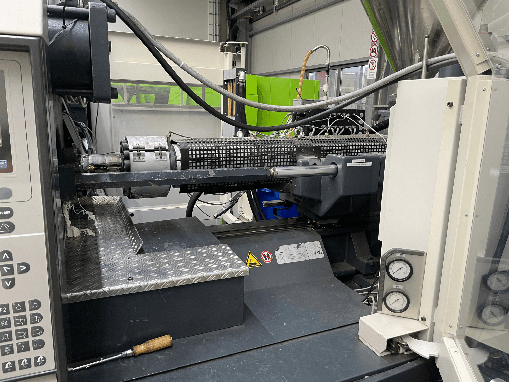 Machine de moulage par injection vue de côté avec panneau de commande, extrudeuse et manomètres visibles, idéale pour les tâches de fabrication.