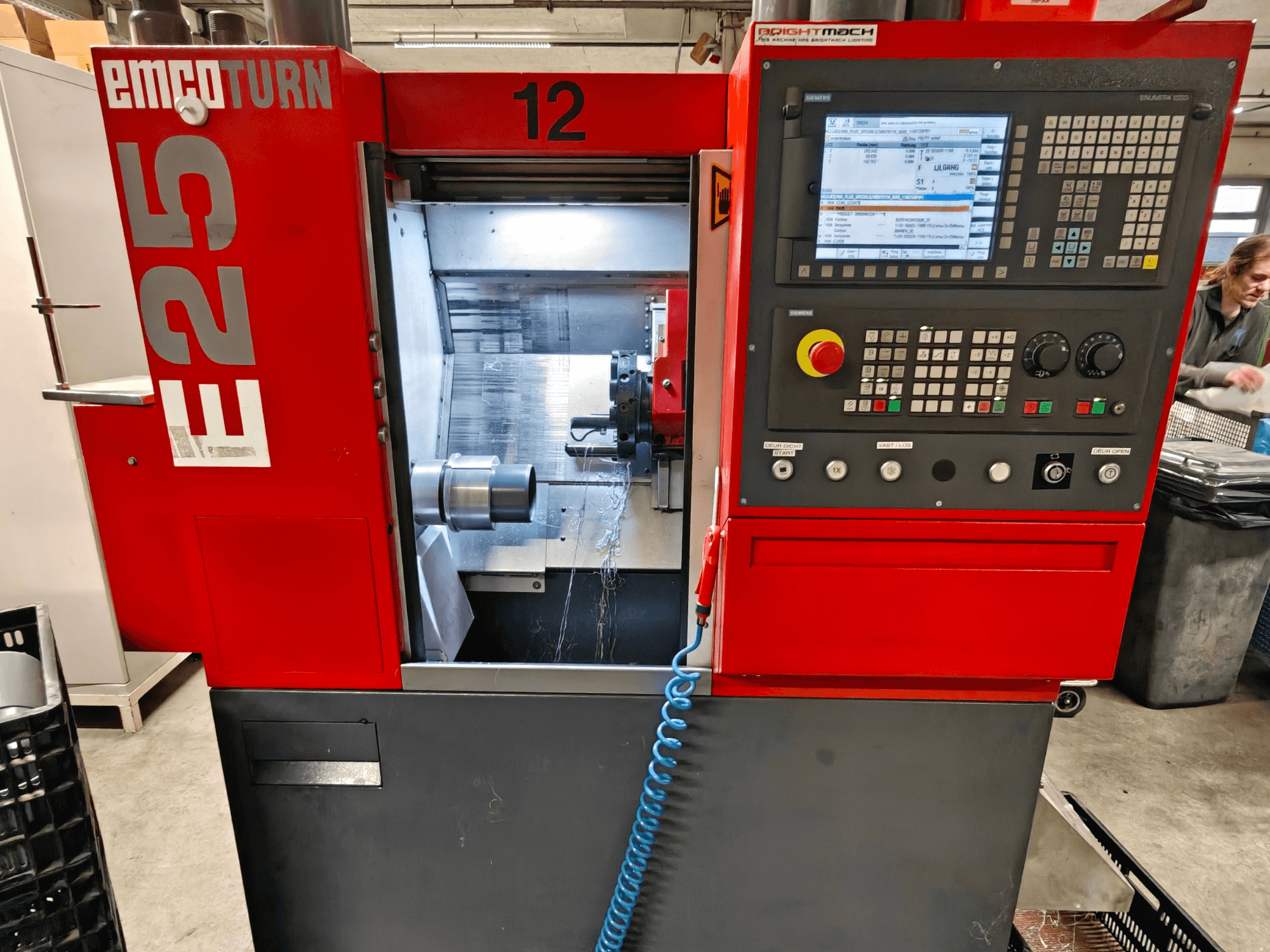 Vue avant de la machine EMCO TURN E25, avec le panneau de commande, le porte-outil et la zone intérieure avec l'outil de coupe visible.