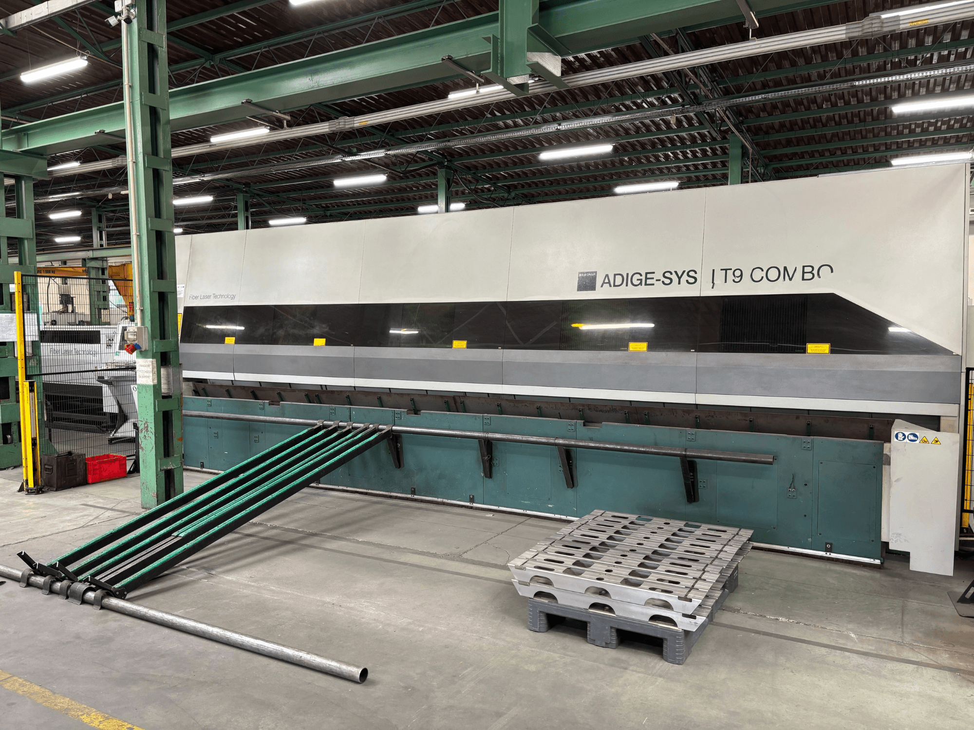 Vue de face de la machine de découpe de tubes BLM Adige LT9 Combo, avec ses bras de chargement verts et sa palette, dans l'atelier de production.