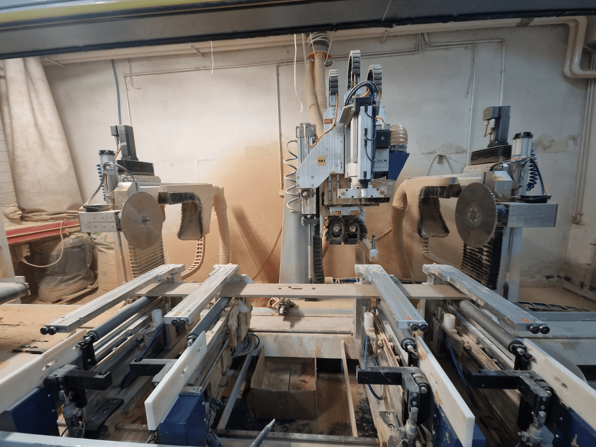 Machine CNC avec deux lames de scie et rails, vue de face. Systèmes d'extraction de la poussière visibles, adaptés au travail du bois.