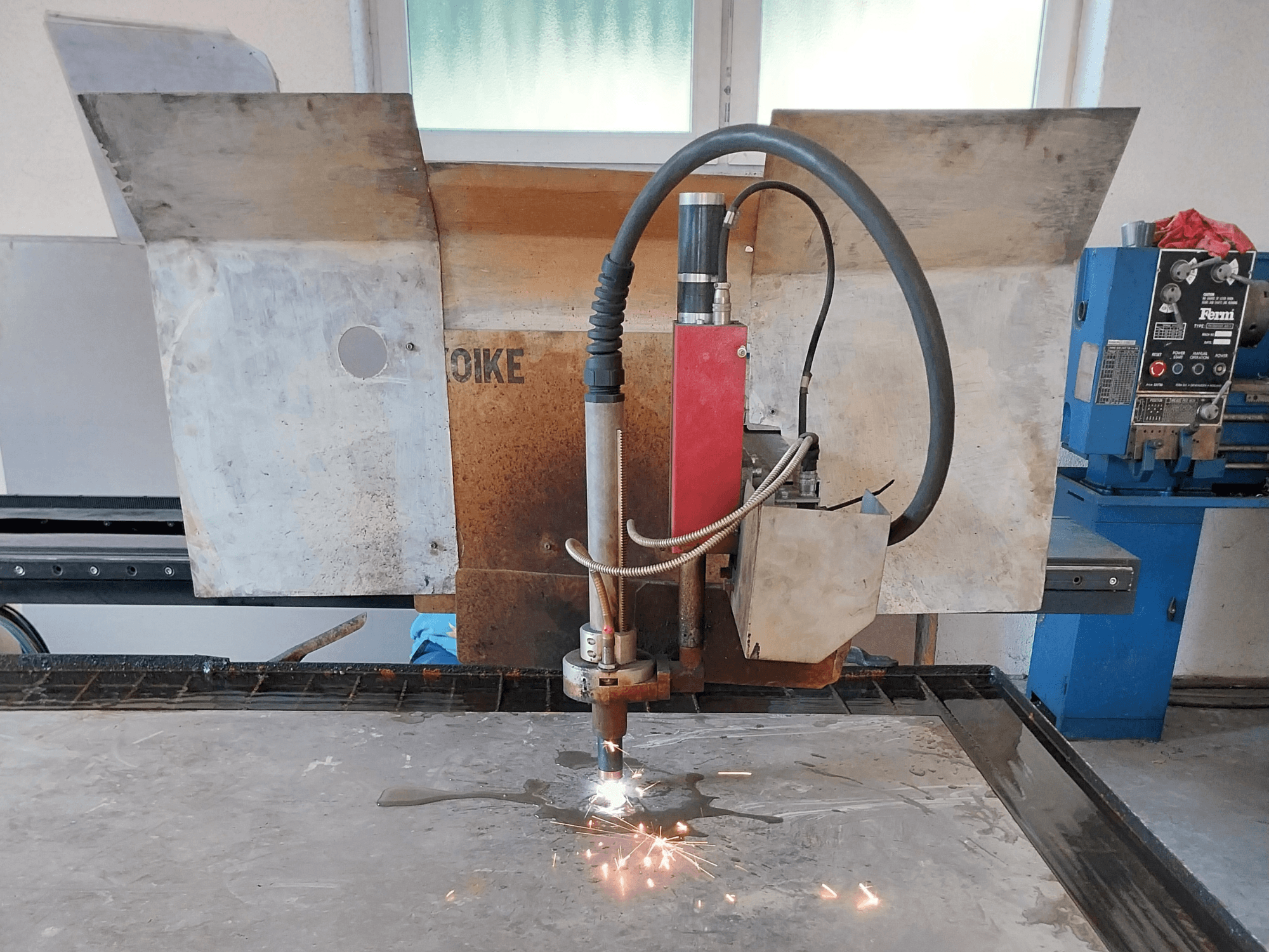 Vue de face d'un découpeur plasma Oike avec des étincelles, positionné au-dessus d'une surface métallique sur une table de travail.