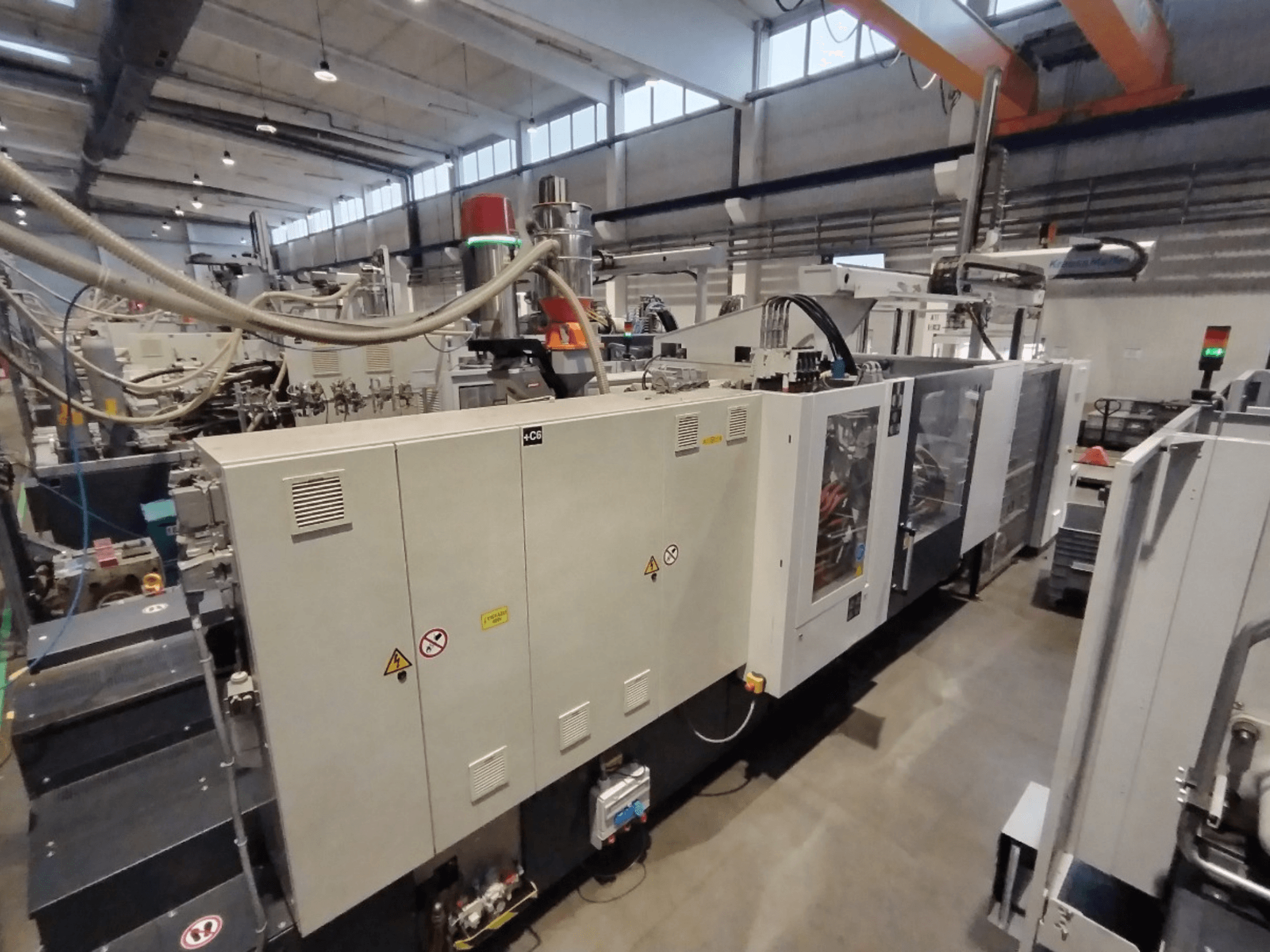 Machine industrielle de moulage par injection, vue de côté, avec panneau de commande et avertissements de sécurité. Marque : Inconnu.