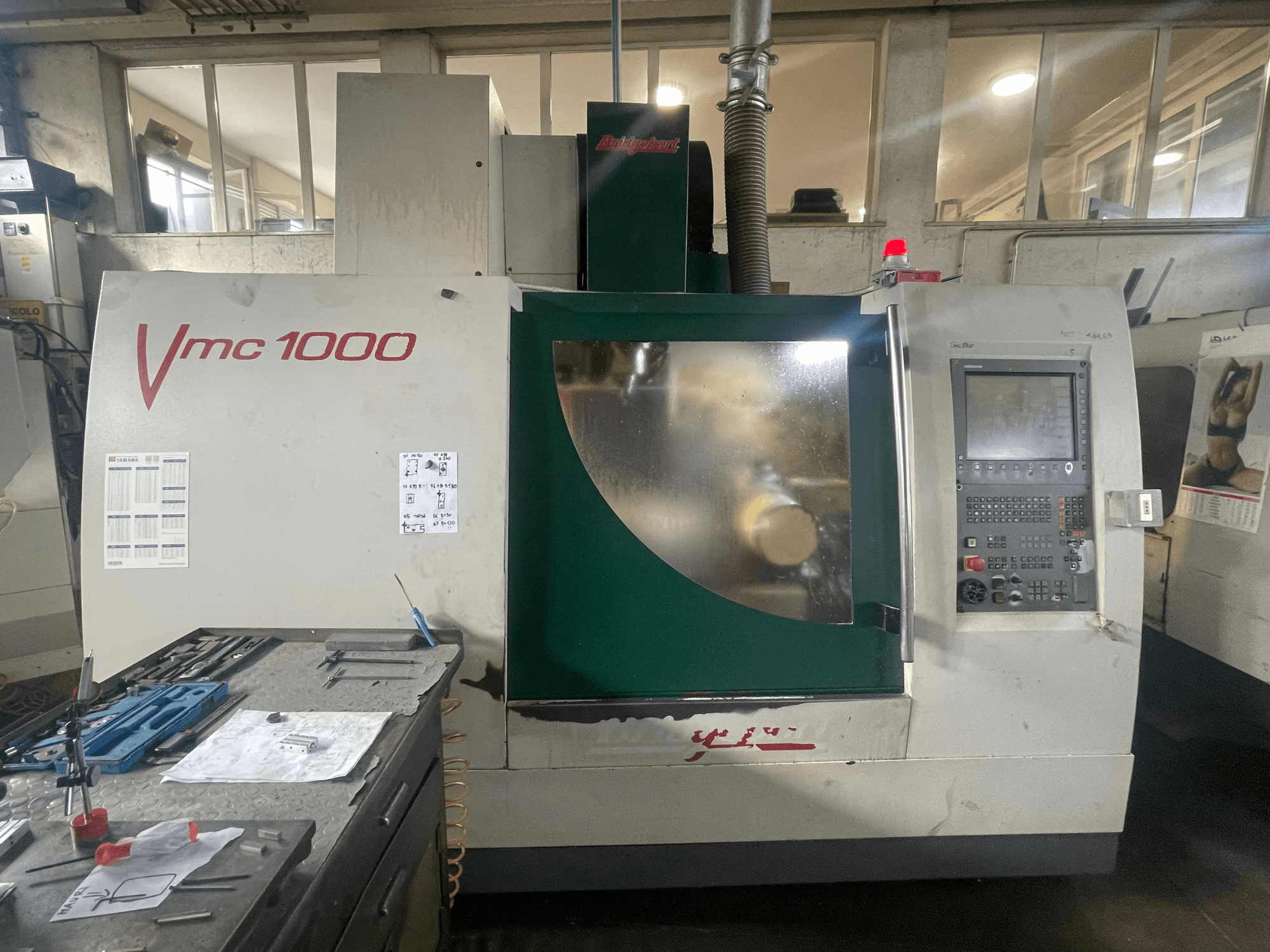 Centre d'usinage vertical Bridgeport VMC 1000/30, vue de face, montrant le panneau de commande et le corps principal, avec des outils à proximité.