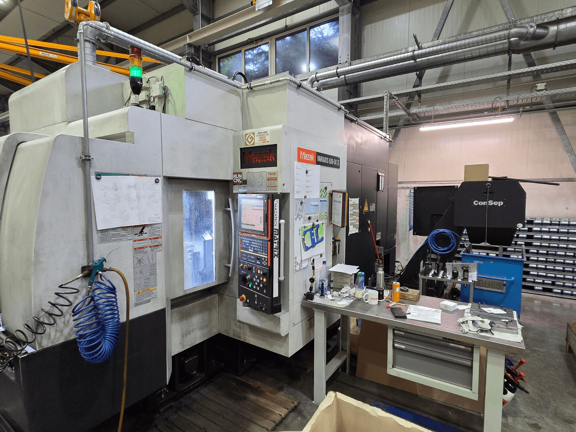 Machine CNC Mazak Variaxis 630-5X dans un atelier, vue de face avec le panneau de commande, le tuyau et les accessoires sur la table latérale.