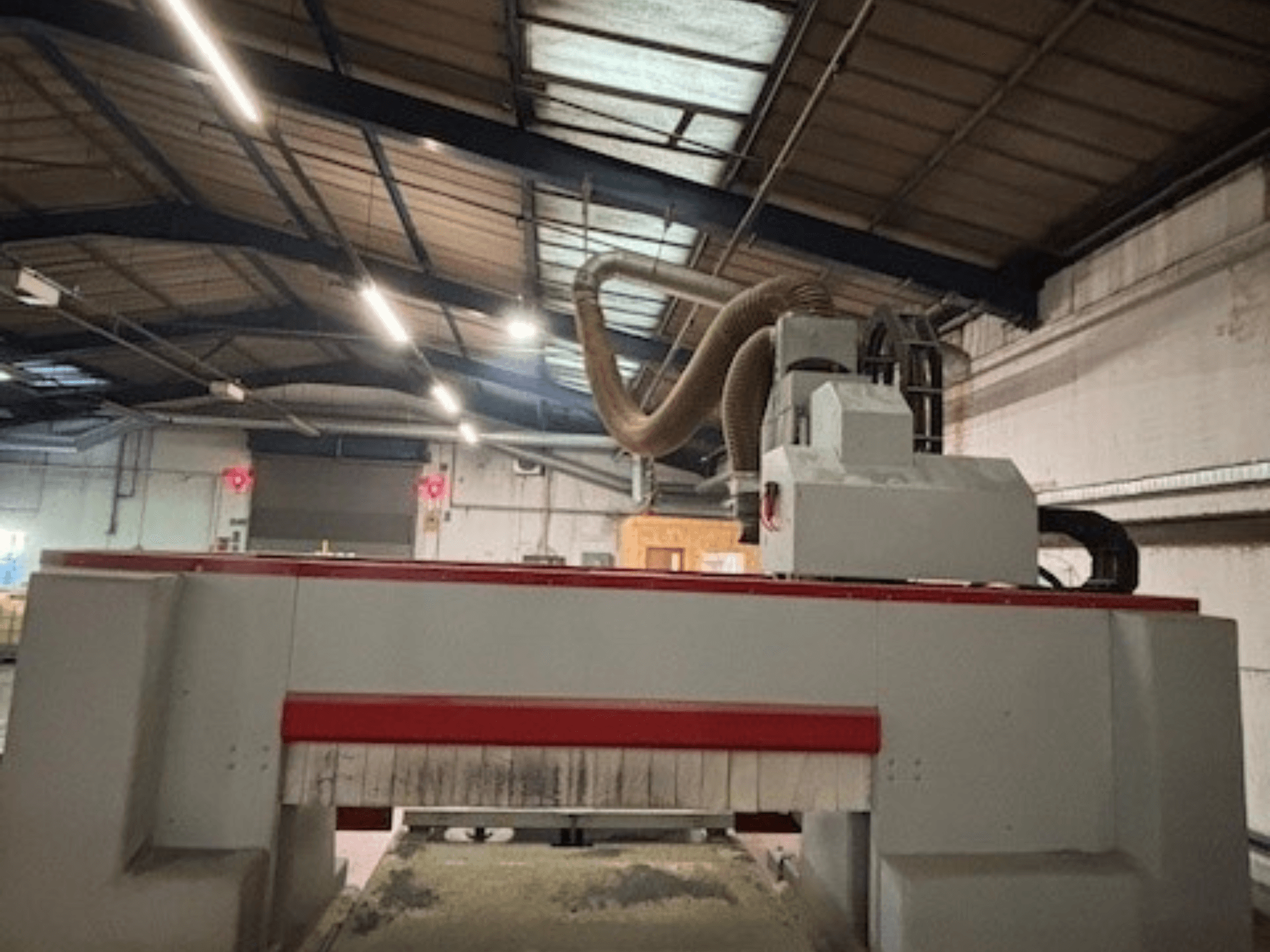 Machine à router CNC dans un atelier, vue de côté mettant en évidence la conception rouge et grise, système d'extraction de la poussière attaché.